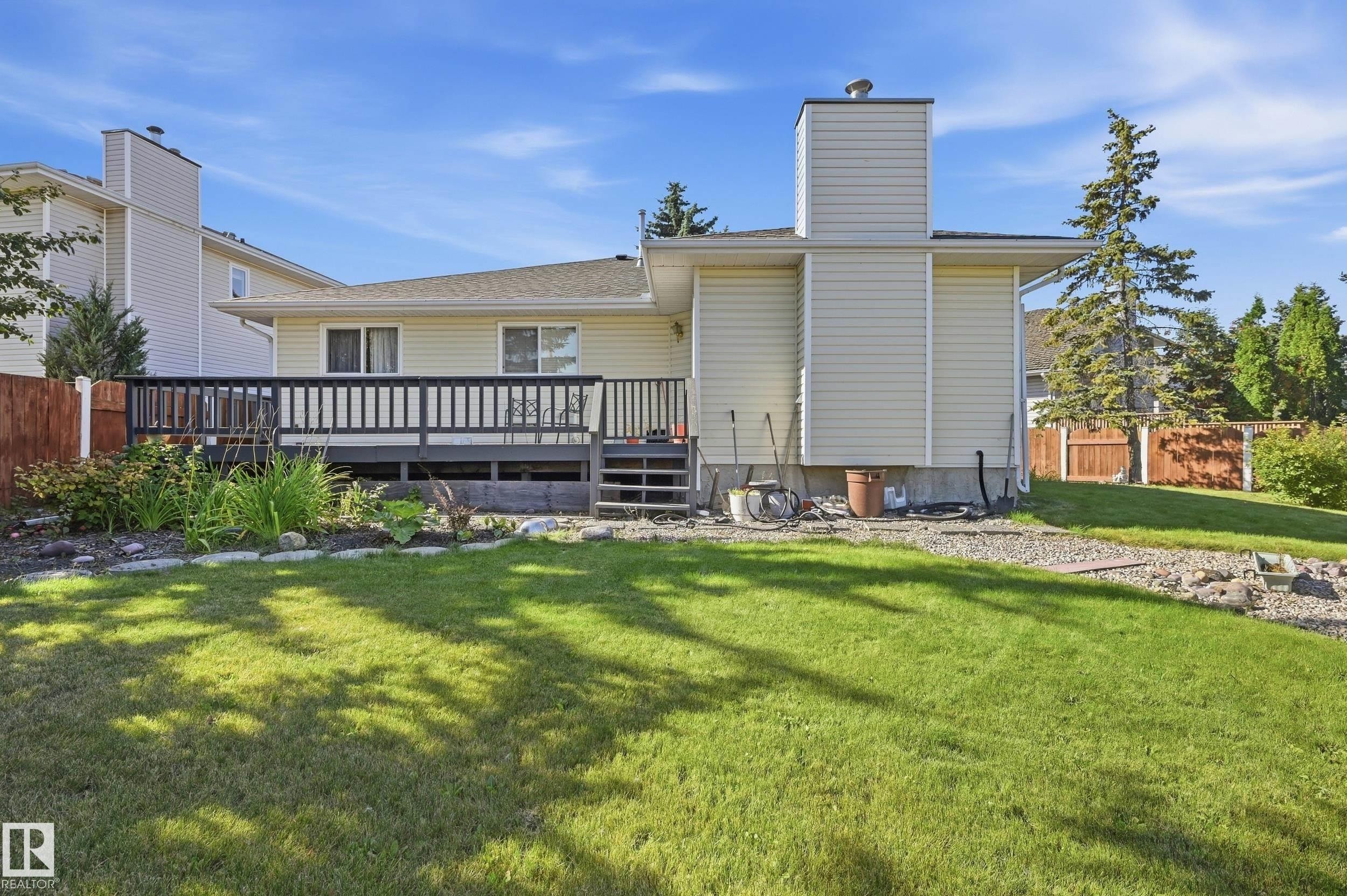 Expansive backyard featuring a manicured lawn, a raised deck with dark railings, exterior siding, and a prominent chimney - 11102 11A Avenue Nw, Edmonton, AB