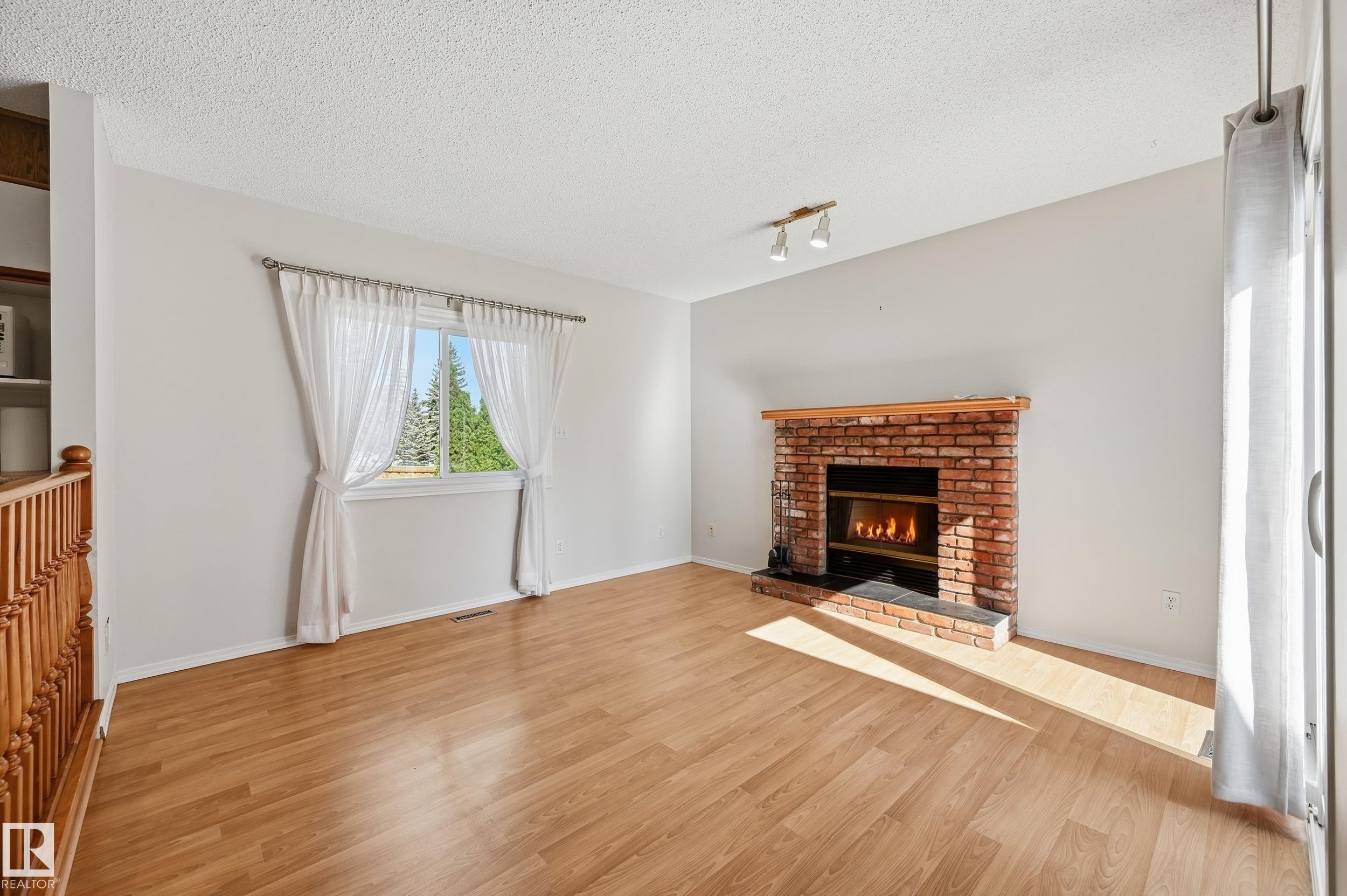 Wood-finish flooring, brick fireplace with a wood mantle, track lighting, and a built-in shelving unit - 11102 11A Avenue Nw, Edmonton, AB