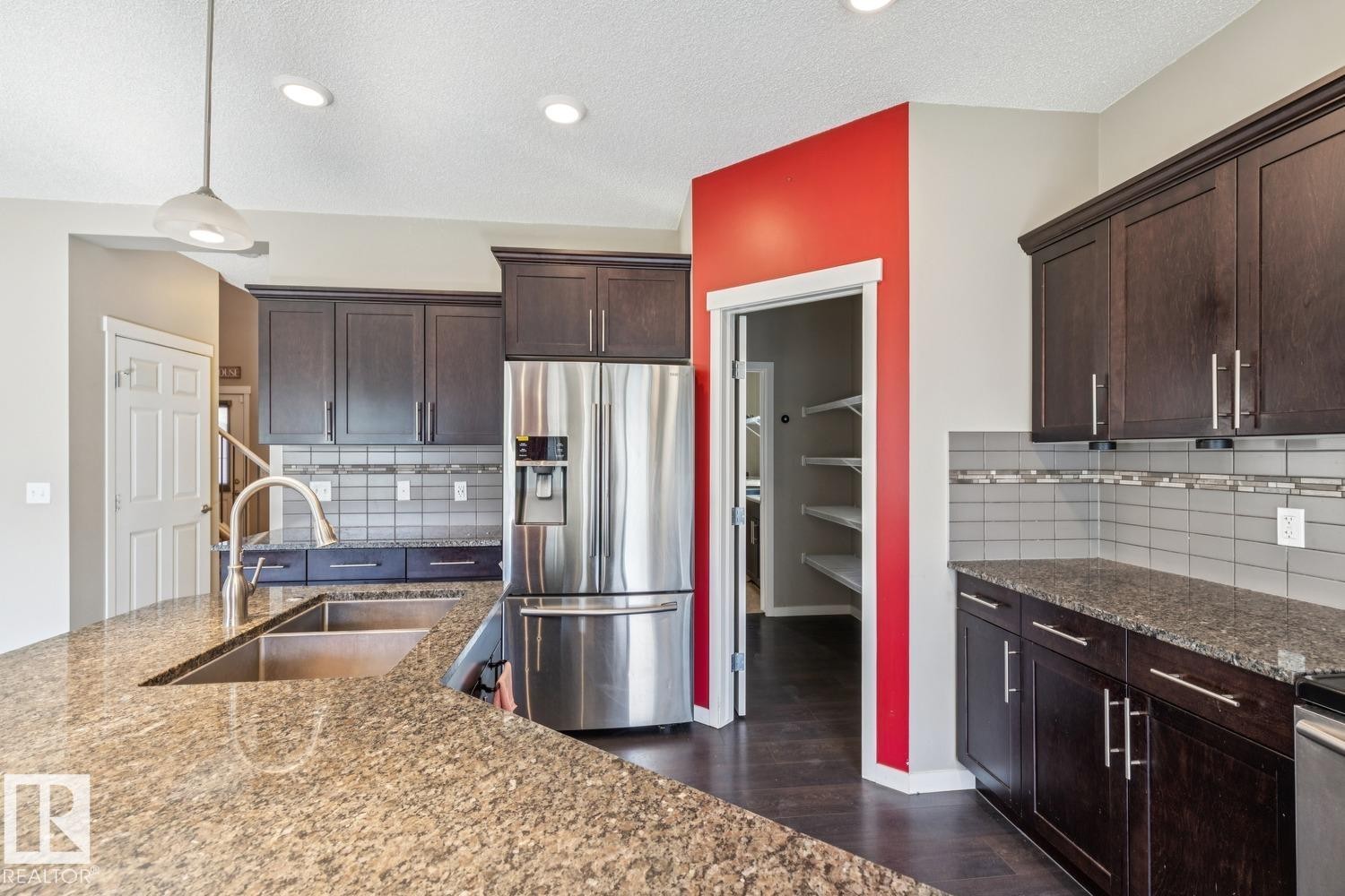 Kitchen featuring rich wood-finish cabinetry, stone countertops, stainless steel appliances, a tile backsplash, and a pantry with built-in shelving - 12007 173 Avenue Nw, Edmonton, AB