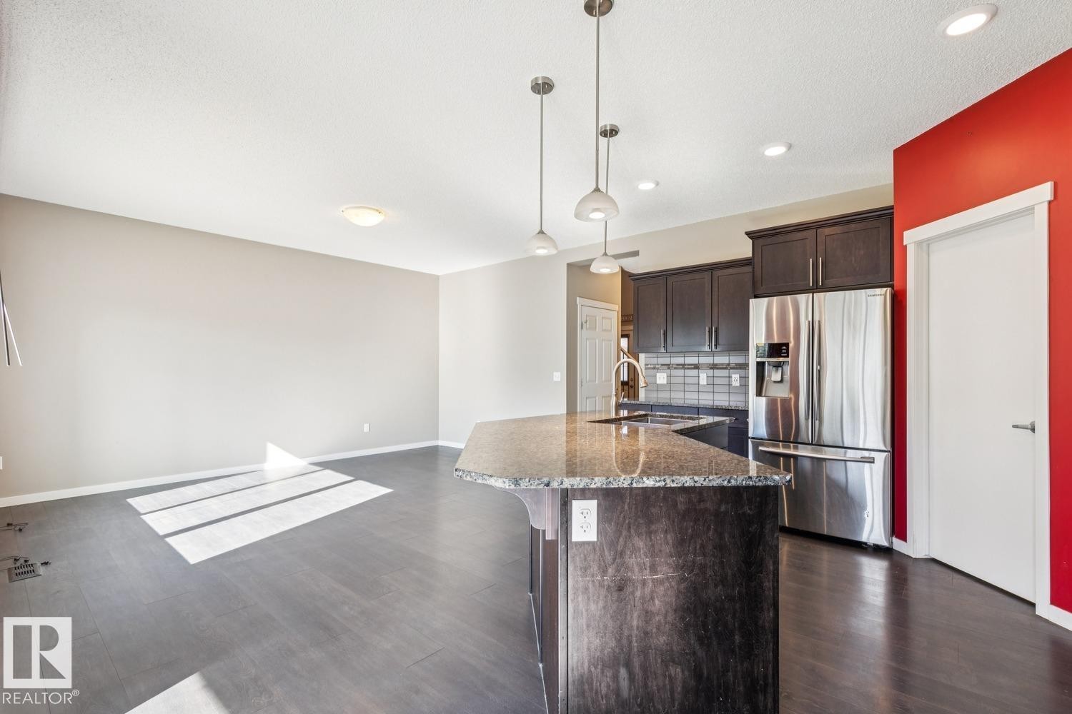 Kitchen island with a granite countertop, dark wood-finish cabinetry, stainless steel refrigerator, and pendant lighting fixtures - 12007 173 Avenue Nw, Edmonton, AB