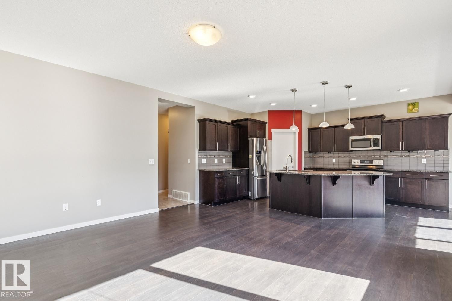 Spacious kitchen featuring dark wood cabinetry, a central island with a sink, stainless steel appliances, and pendant lighting - 12007 173 Avenue Nw, Edmonton, AB