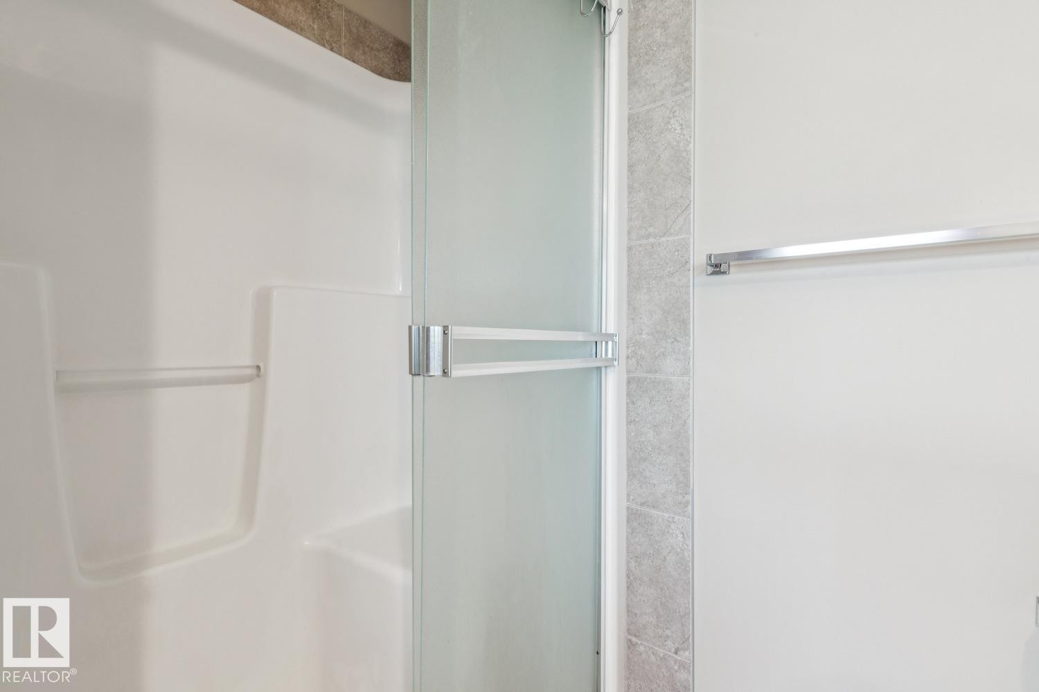 Shower with a frosted glass door, an integrated grab bar, and light-toned wall tiling - 12007 173 Avenue Nw, Edmonton, AB