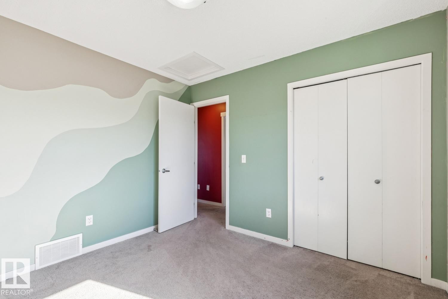 Plush carpet flooring, a wall with decorative wave-patterned paint, a solid white door, and bi-fold closet doors - 12007 173 Avenue Nw, Edmonton, AB