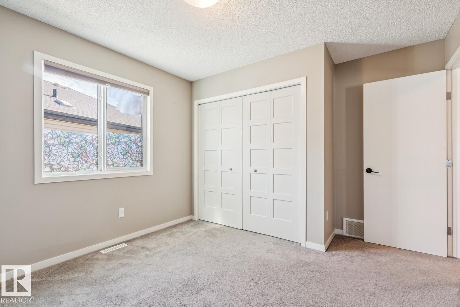 Neutral tone wall paint, textured ceiling, gray carpeting, dual-pane window, and white paneled bi-fold closet doors - 12007 173 Avenue Nw, Edmonton, AB