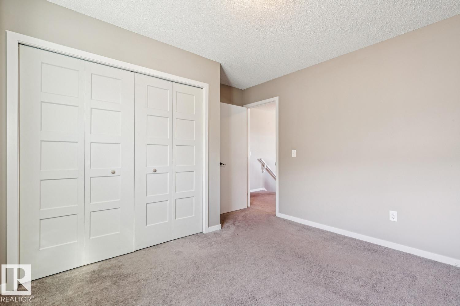 Neutral wall color, wall-to-wall carpeting, bi-fold closet doors with square paneling, white trim, and a textured ceiling - 12007 173 Avenue Nw, Edmonton, AB