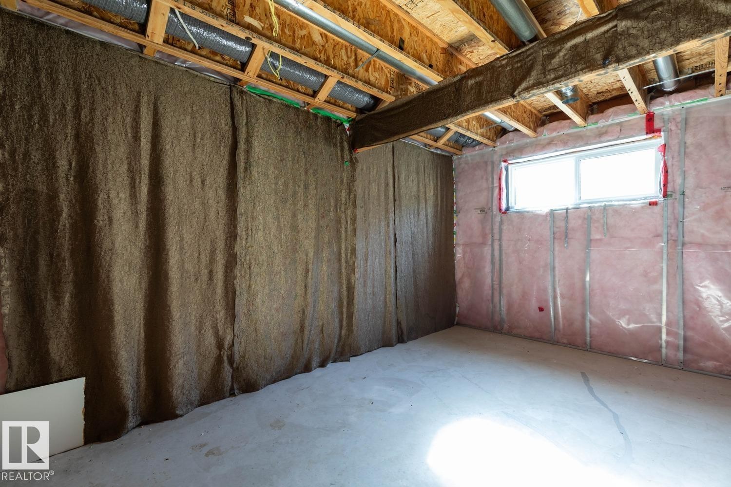 Unfinished basement space featuring exposed wood joists, concrete flooring, and an egress window - 12007 173 Avenue Nw, Edmonton, AB