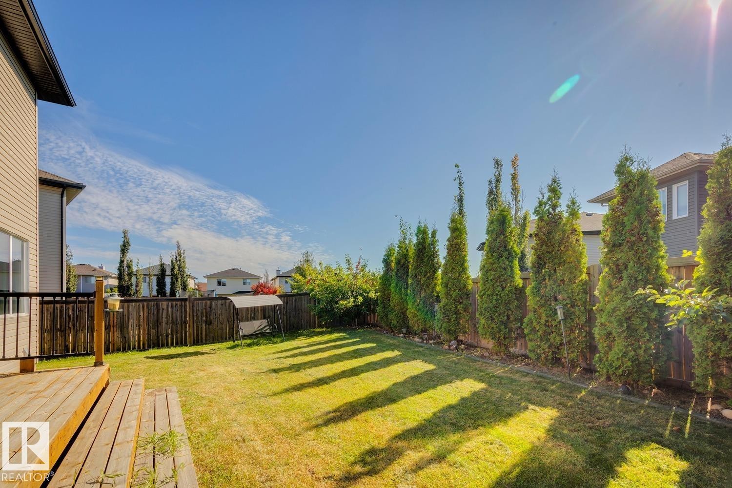 Expansive backyard featuring a wood deck, manicured lawn, and privacy fencing with mature trees - 12007 173 Avenue Nw, Edmonton, AB