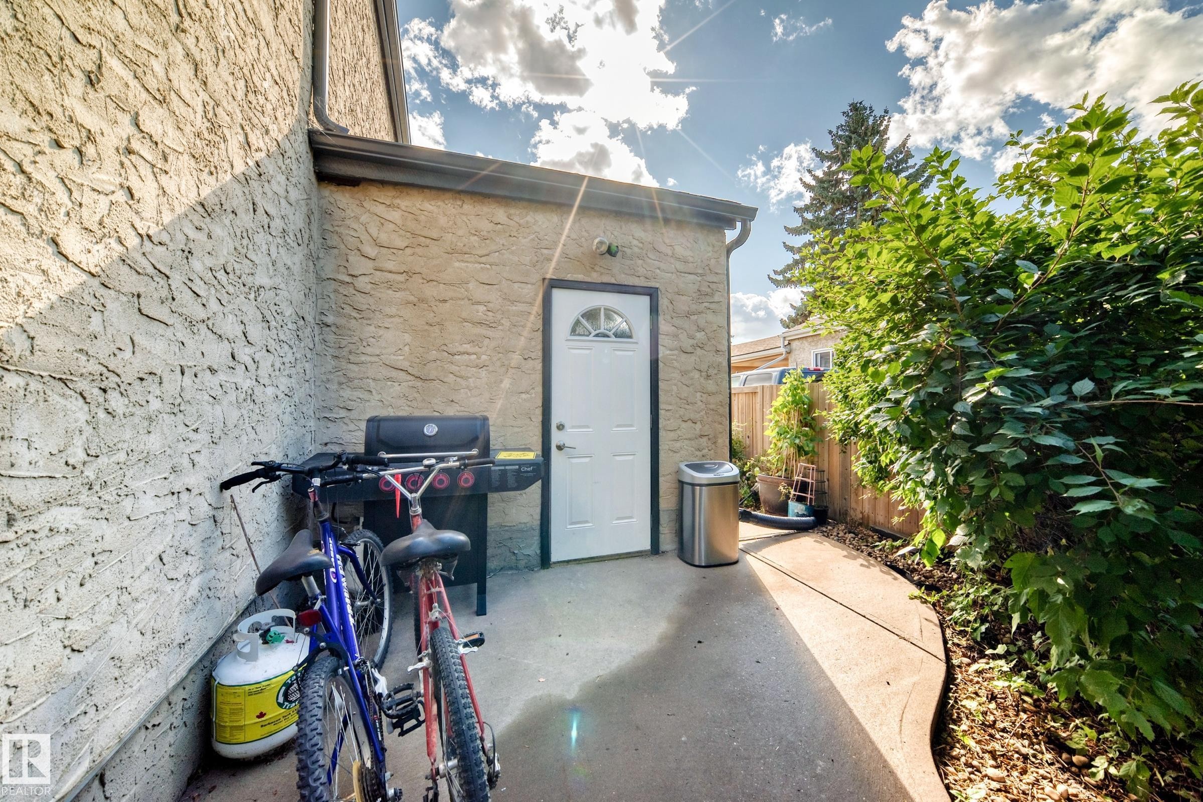 Concrete patio area featuring a white exterior door with an arched window, stucco exterior wall, and a wood fence - 5620 93A Avenue Nw, Edmonton, AB