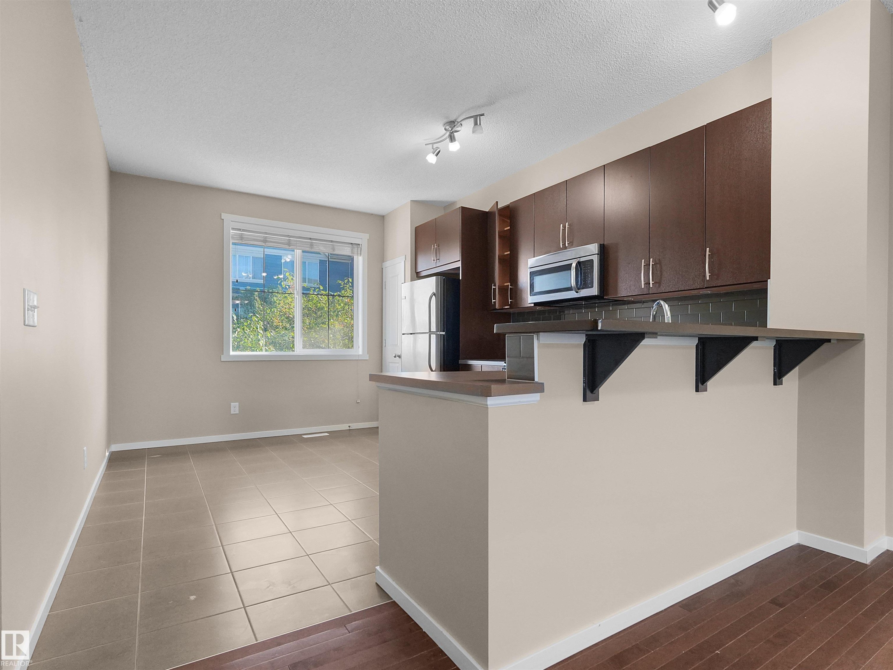 Kitchen with dark wood cabinetry, stainless steel microwave, and an extended breakfast bar - #162 603 Watt Bv Sw, Edmonton, AB