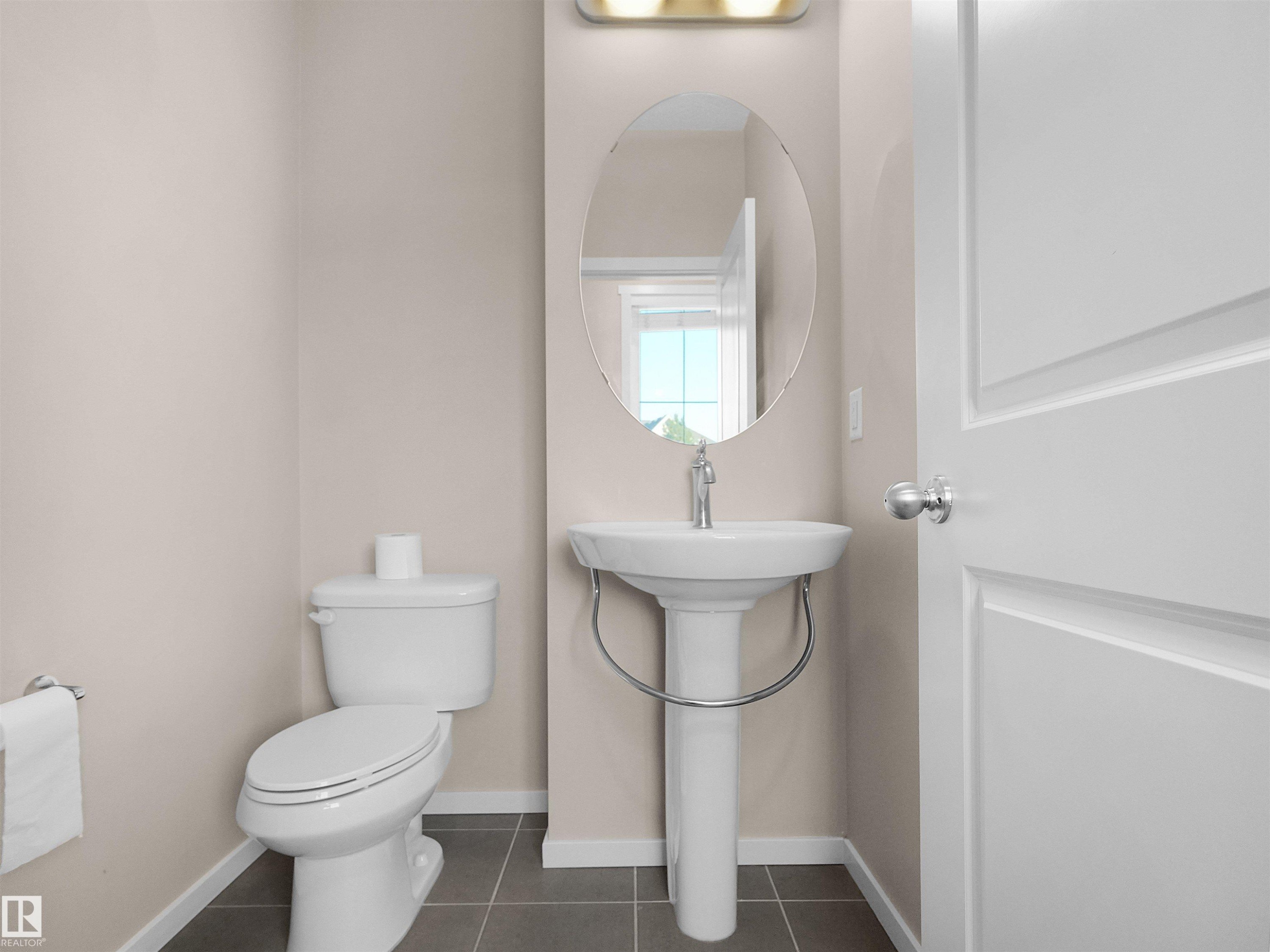 Powder room featuring a pedestal sink, oval mirror, wall-mounted light fixture, and tile flooring - #162 603 Watt Bv Sw, Edmonton, AB