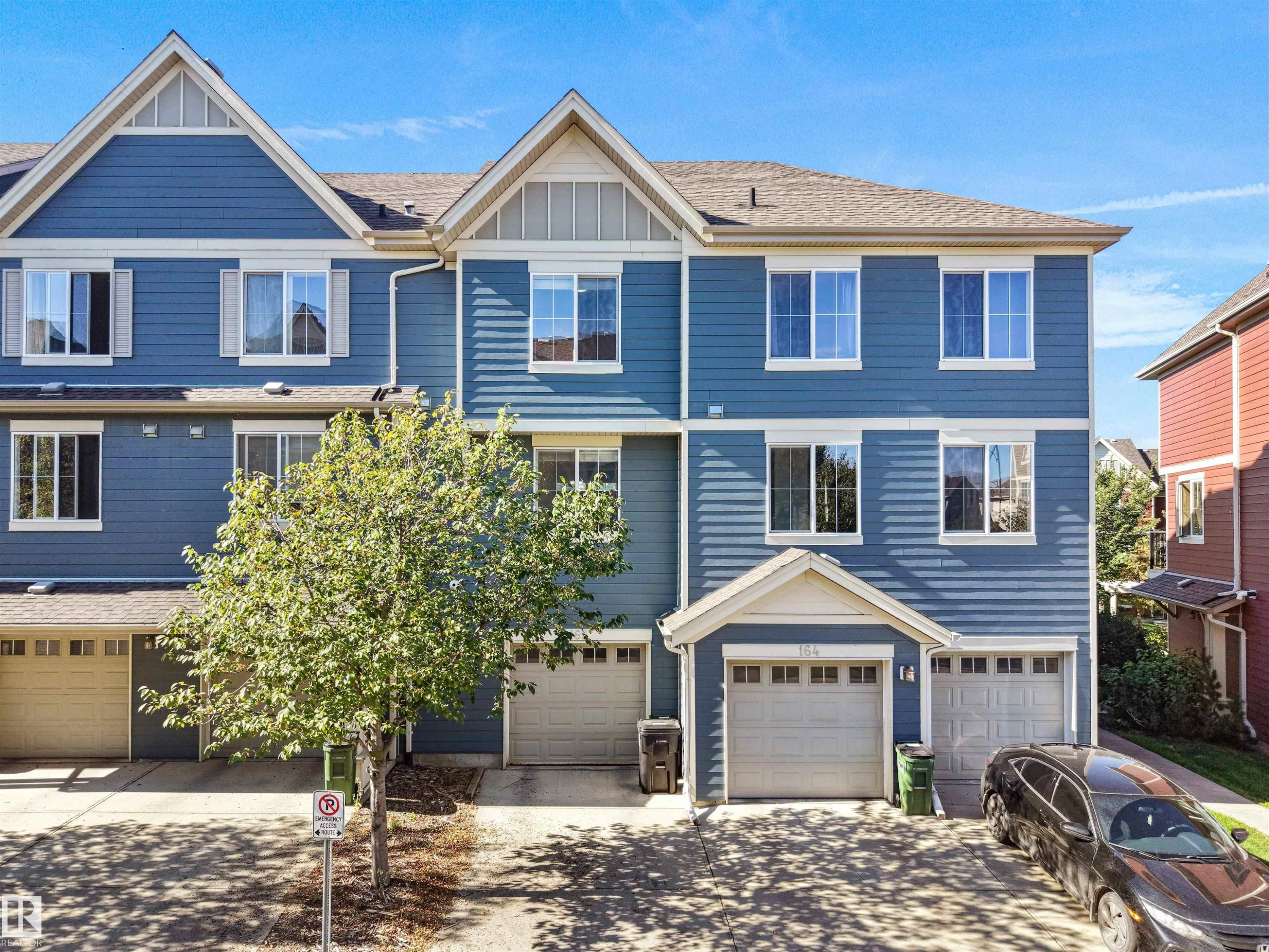 Blue siding exterior with white window trim, multiple windows, and two attached garages - #162 603 Watt Bv Sw, Edmonton, AB