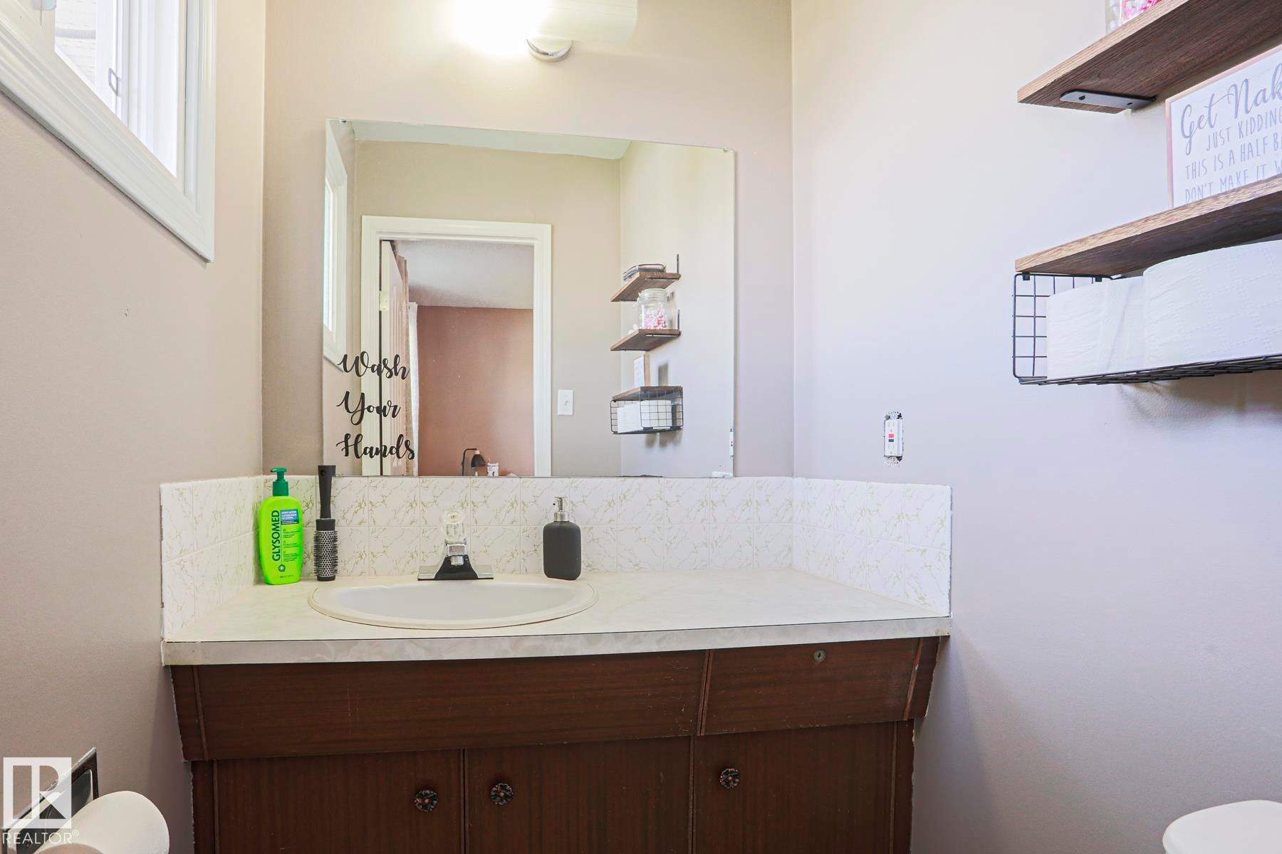 Bathroom featuring a wood-finish vanity with a built-in sink, a wall-mounted mirror, and overhead lighting - 21 Burlington Avenue, Spruce Grove, AB