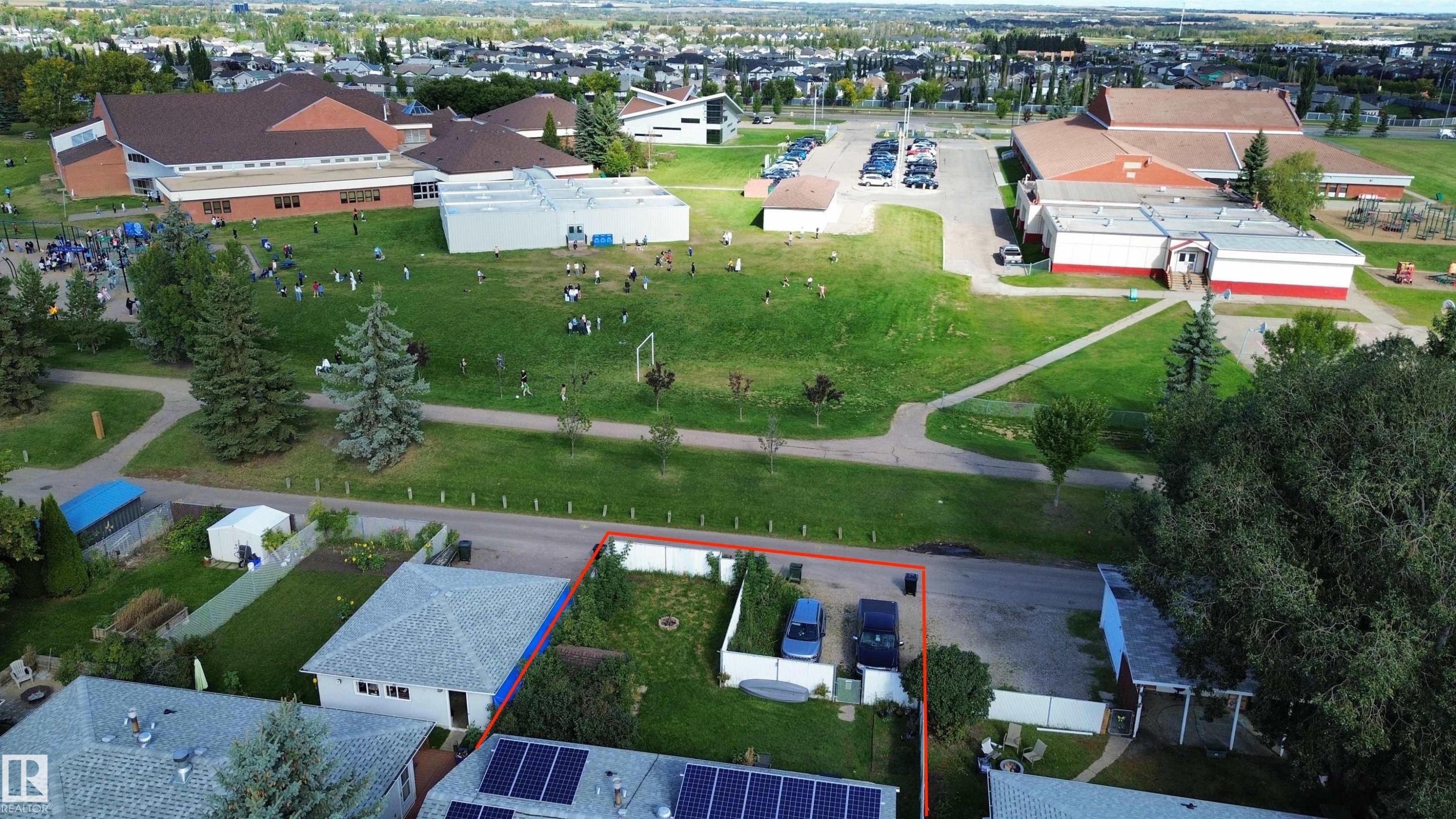Grassy parcel with paved access, featuring a white privacy fence and mature trees - 21 Burlington Avenue, Spruce Grove, AB