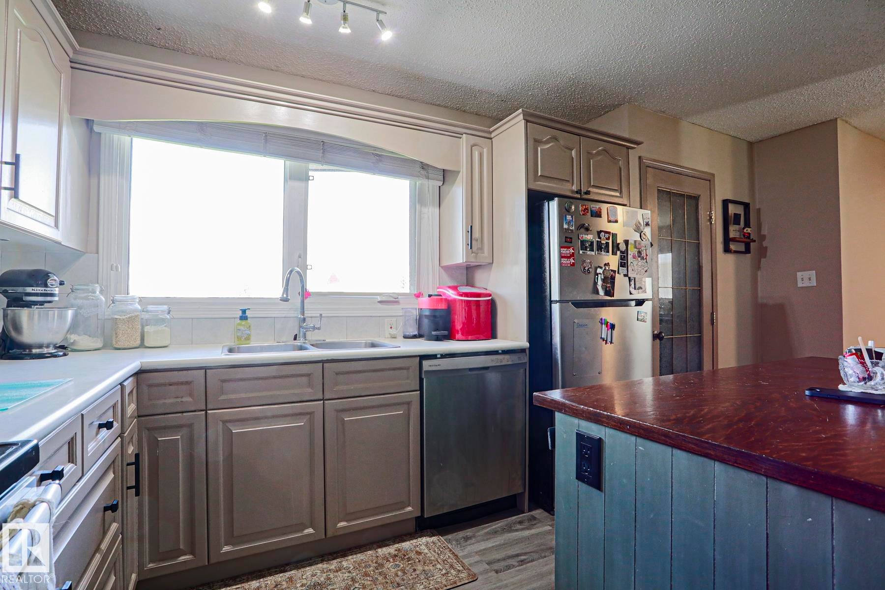Kitchen featuring light-toned upper cabinetry, darker lower cabinetry, stainless steel appliances, a center island with a wood-finish countertop, and wood-finish flooring - 21 Burlington Avenue, Spruce Grove, AB
