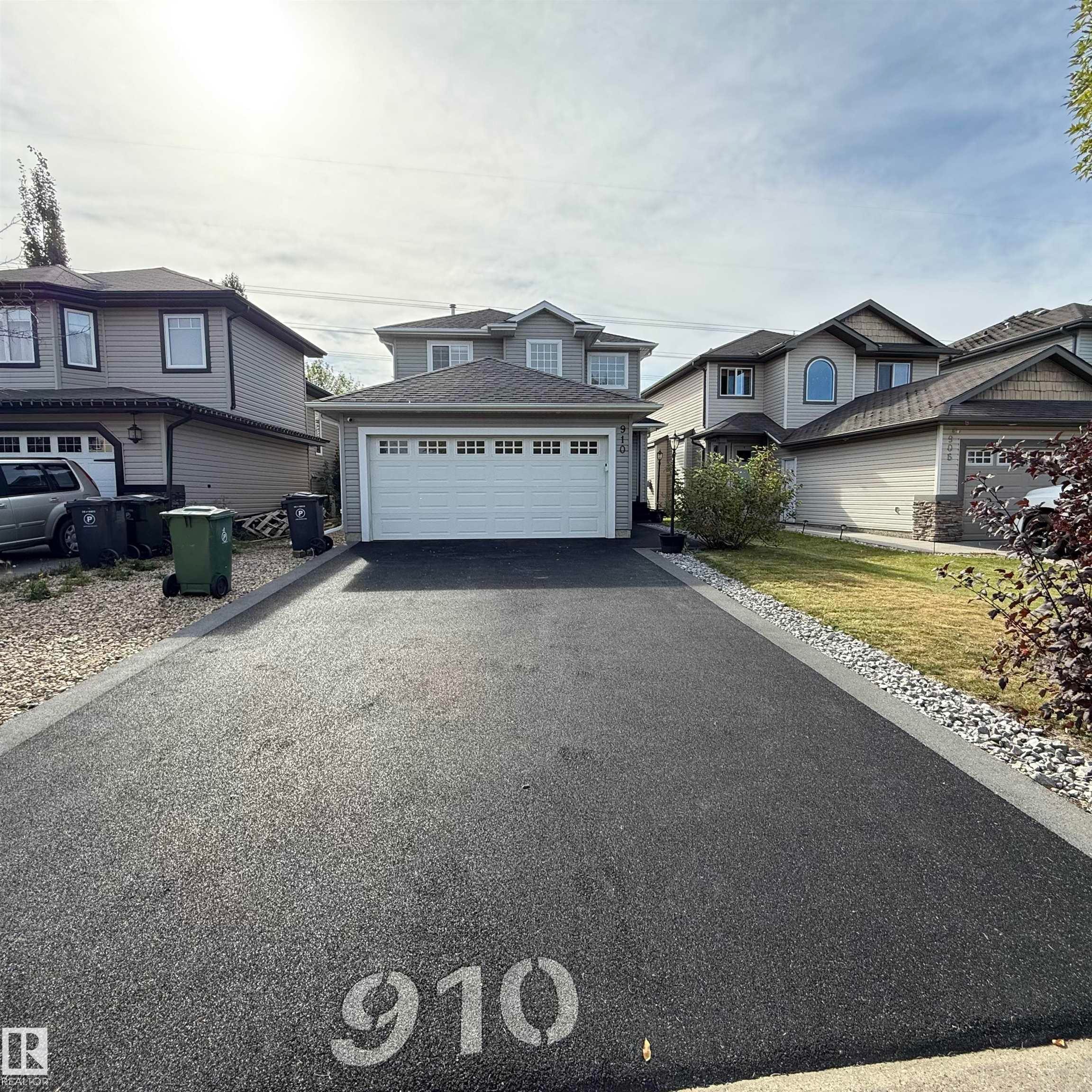 Attached front-facing garage with a multi-pane door, asphalt driveway, and a landscaped yard with established plantings - 910 Oakland Boulevard, Devon, AB