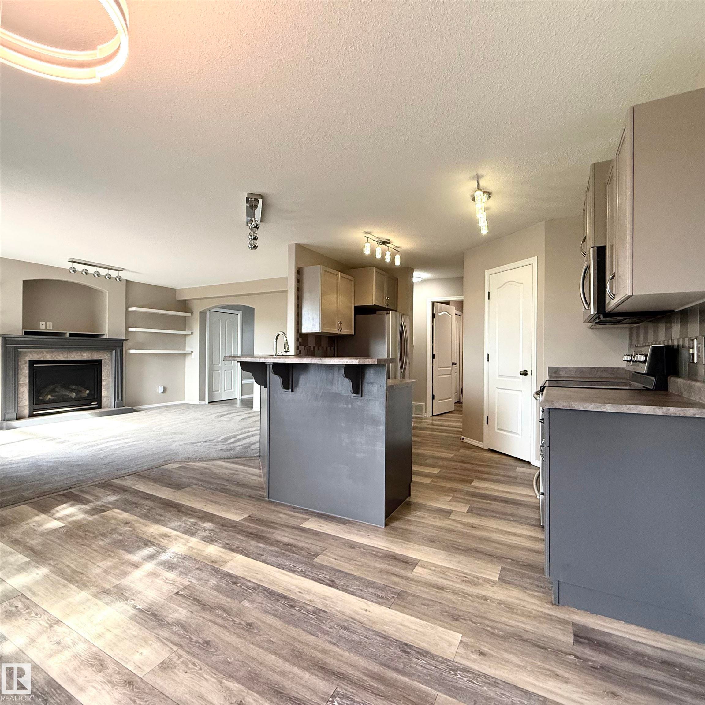 Wood-finish flooring, built-in shelving, fireplace, kitchen island with sink, and stainless steel appliances - 910 Oakland Boulevard, Devon, AB