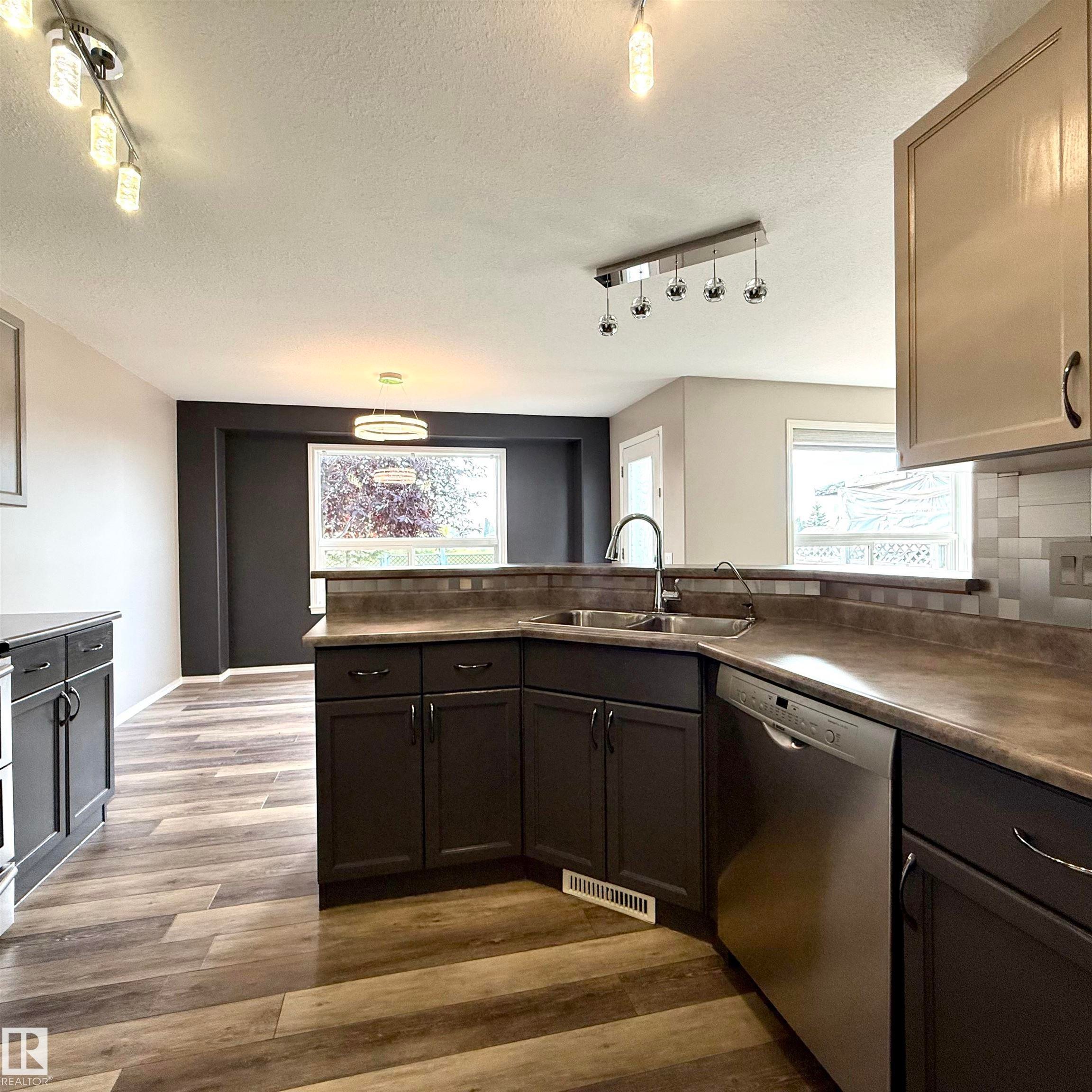 Kitchen featuring stainless steel appliances, dark wood-finish cabinetry, and wood-finish flooring - 910 Oakland Boulevard, Devon, AB