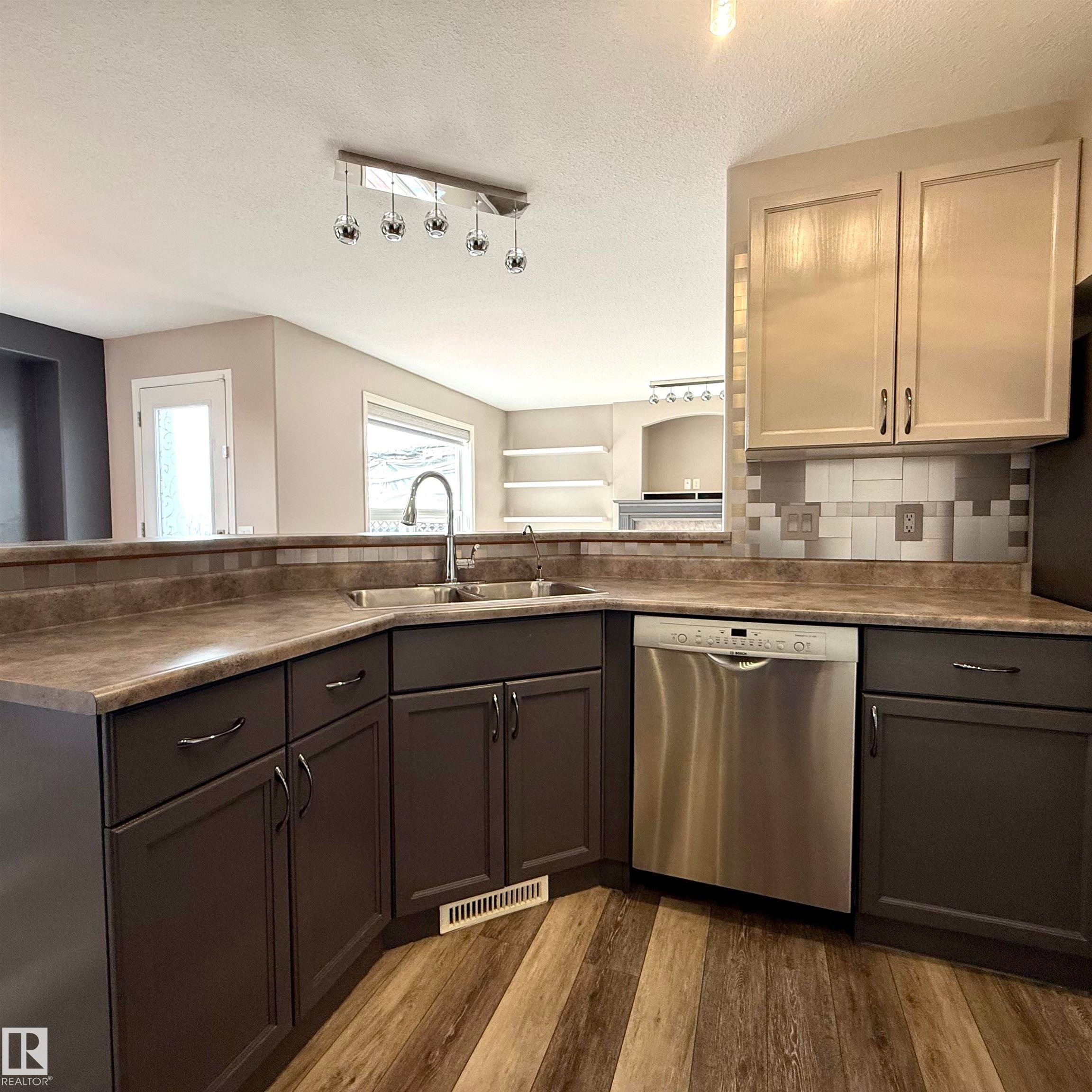 Kitchen featuring wood-finish flooring, dark lower cabinetry, and lighter upper cabinetry - 910 Oakland Boulevard, Devon, AB