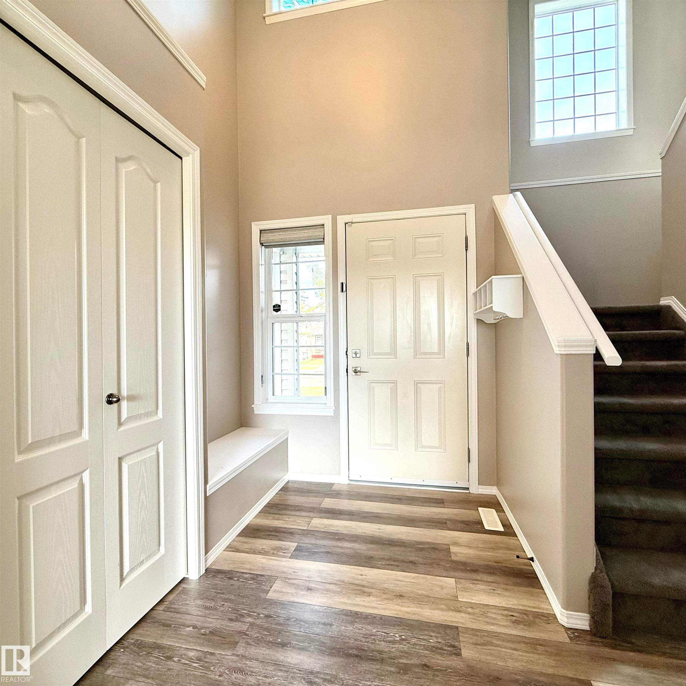Two-story entry foyer with wood-finish flooring, a built-in bench, and a panel-style entry door - 910 Oakland Boulevard, Devon, AB