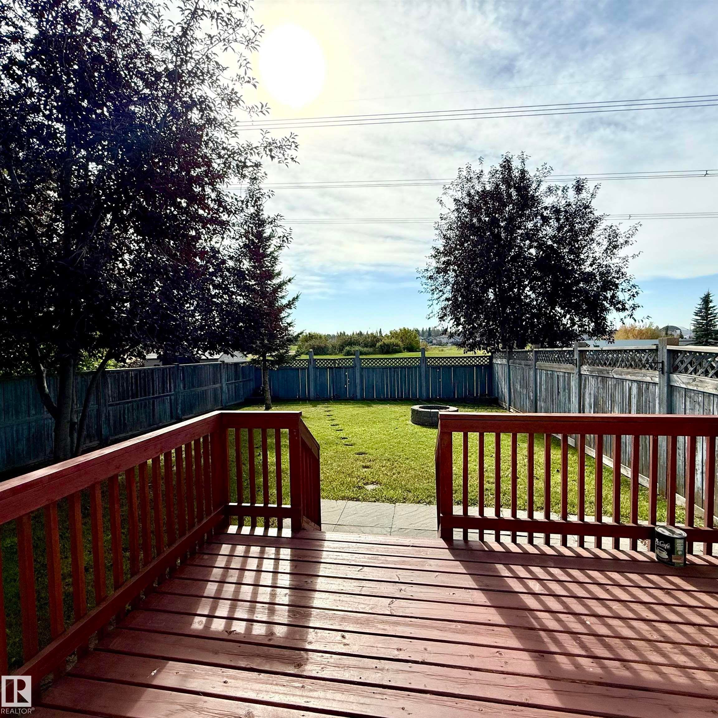 Expansive backyard featuring a wood deck, manicured lawn, and mature trees, surrounded by a privacy fence - 910 Oakland Boulevard, Devon, AB