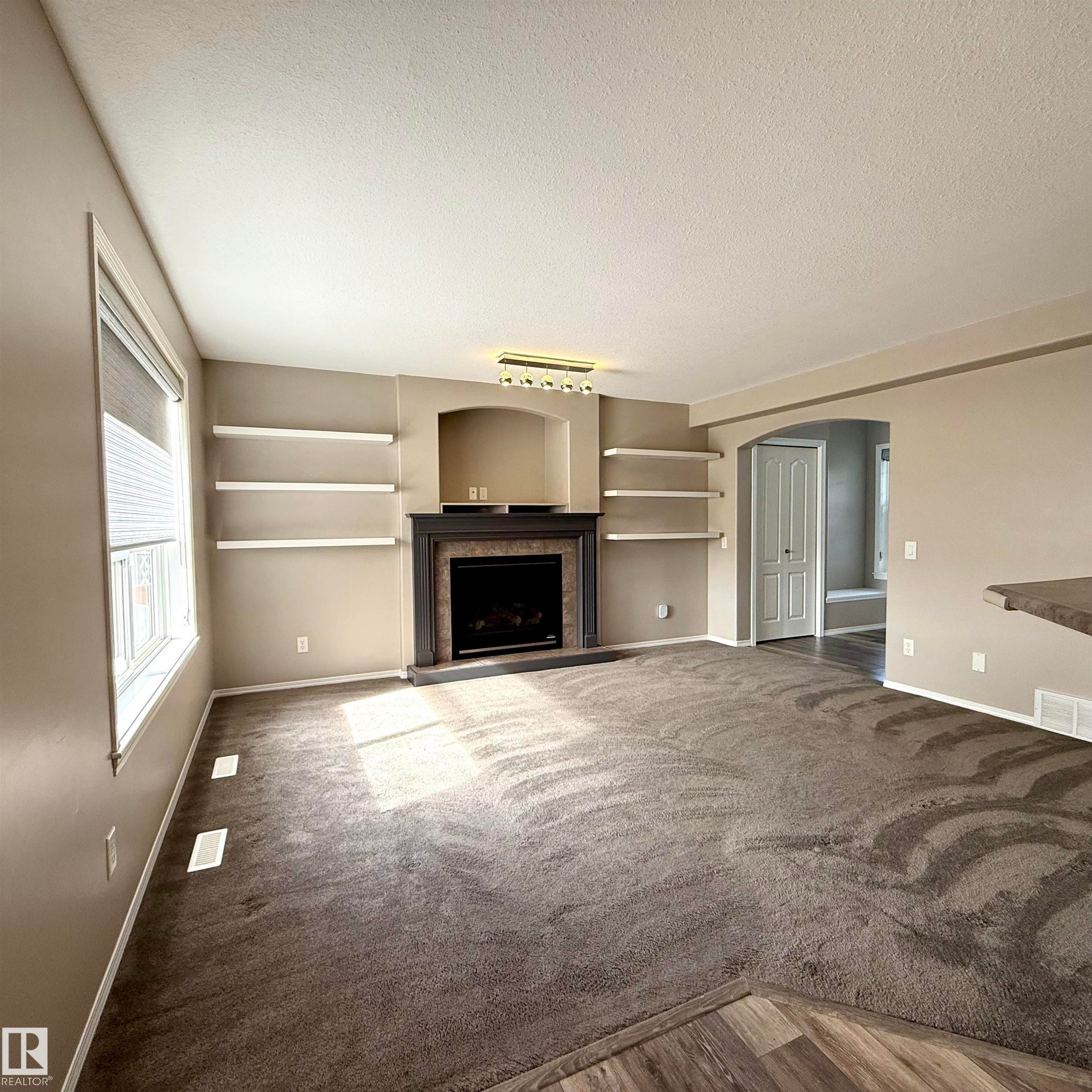Living area featuring a fireplace with a dark wood mantel and surround, built-in shelving, and carpeting - 910 Oakland Boulevard, Devon, AB