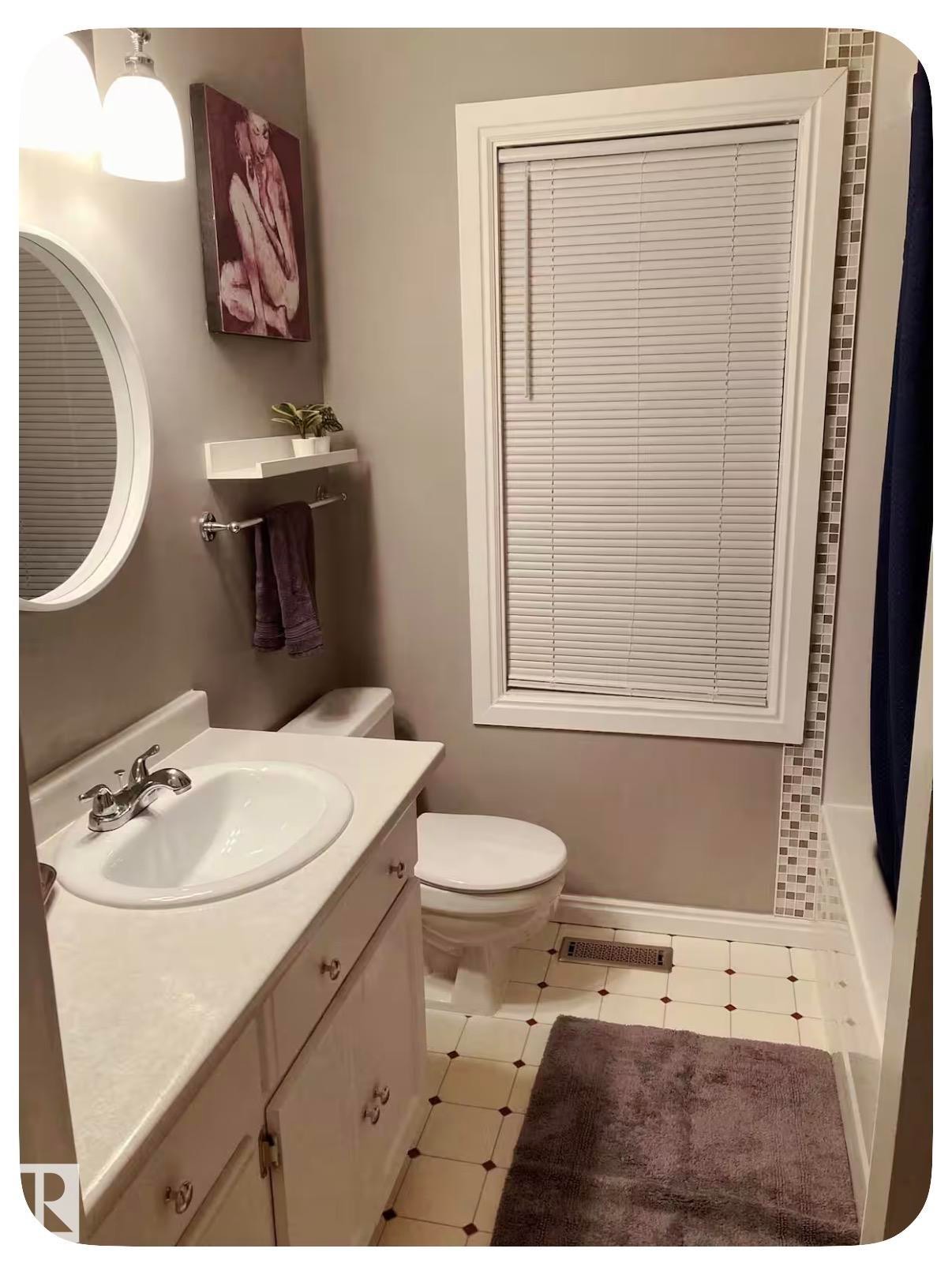 White vanity with an integrated sink, round mirror, and tile flooring - 10649 125 Street Nw, Edmonton, AB