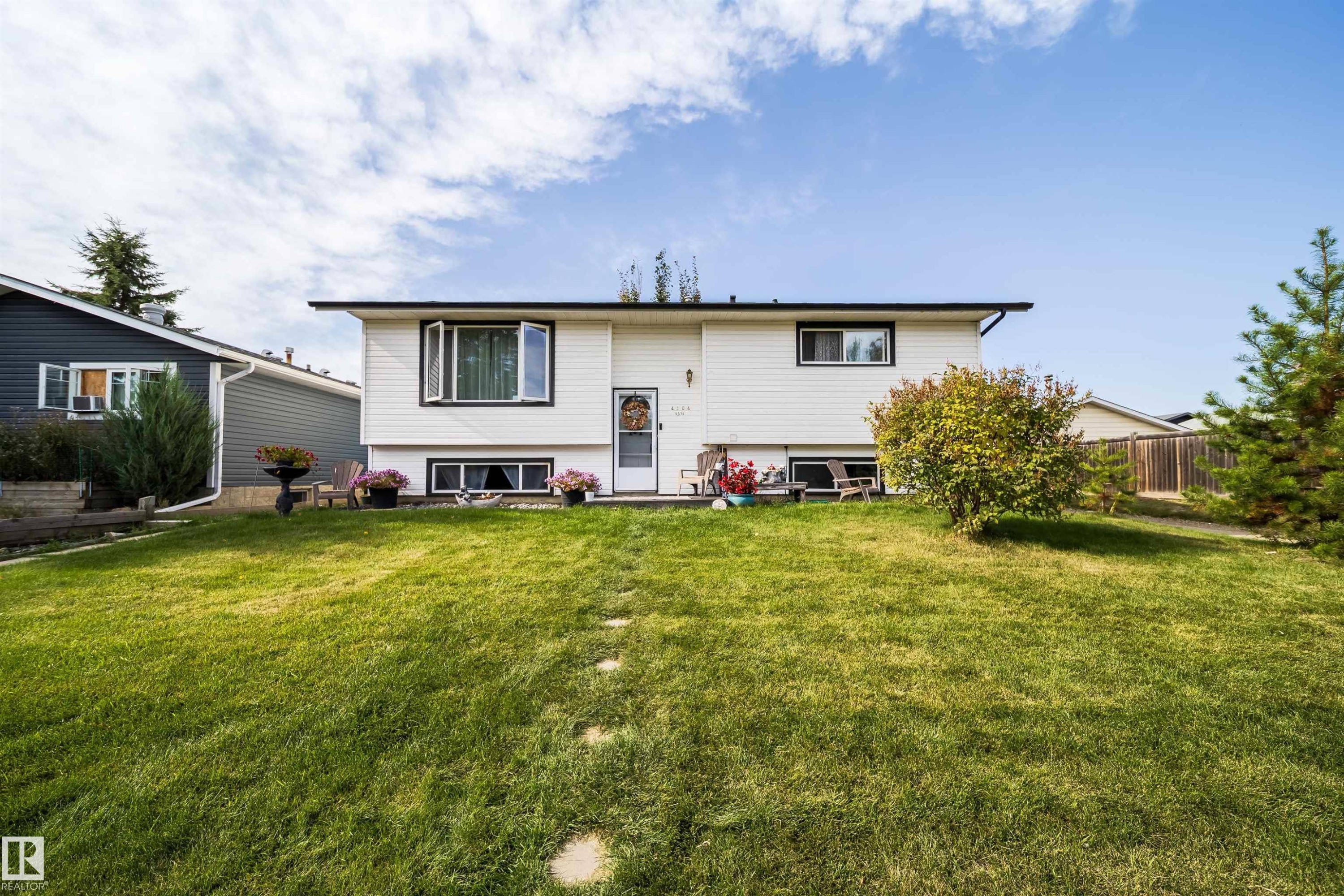 White siding exterior with dark trim accents, front yard with green lawn, and stepping stones - 4104 44 Street, Stony Plain, AB