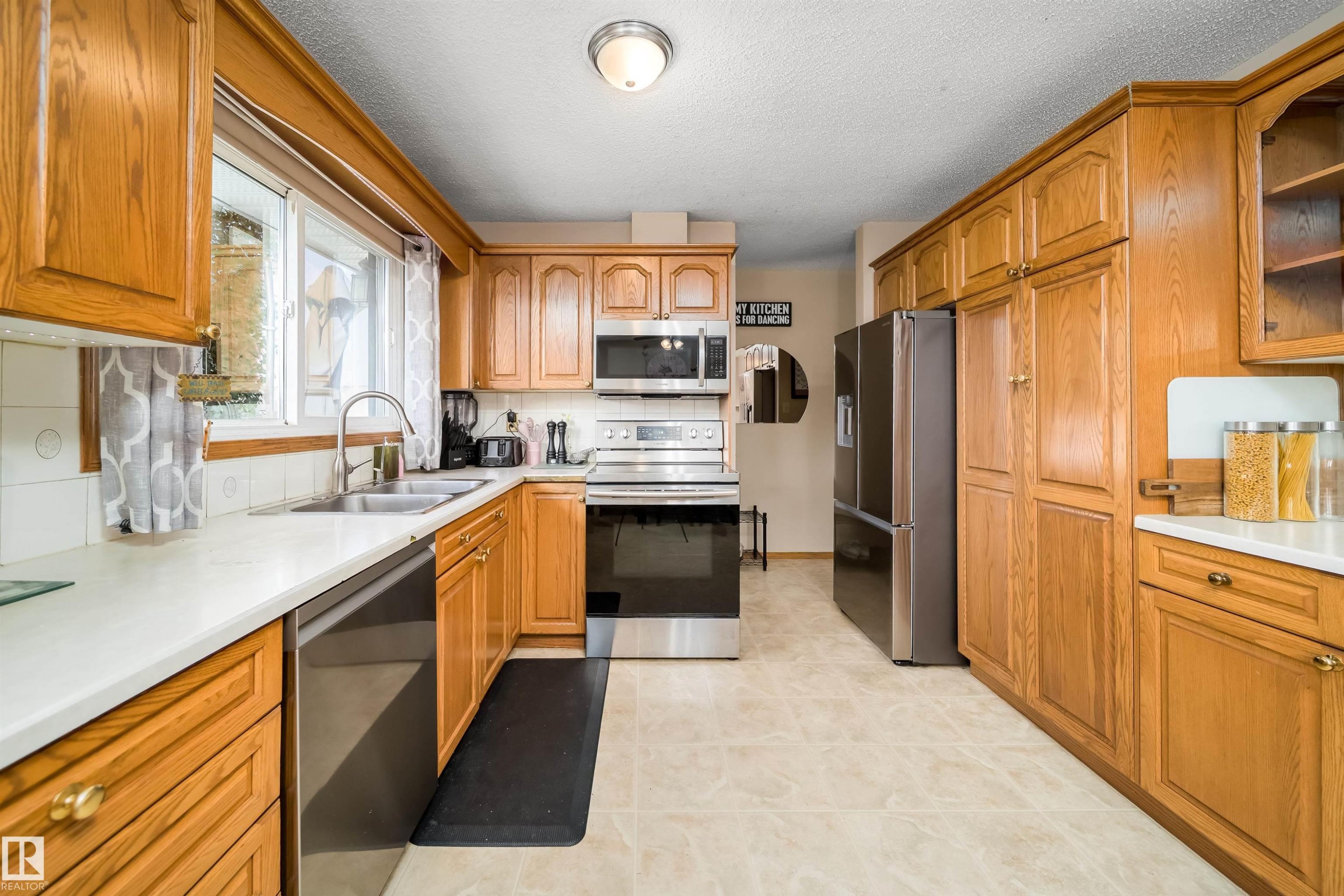 Kitchen featuring wood cabinetry, stainless steel appliances, a double basin sink, and a window above the sink - 4104 44 Street, Stony Plain, AB