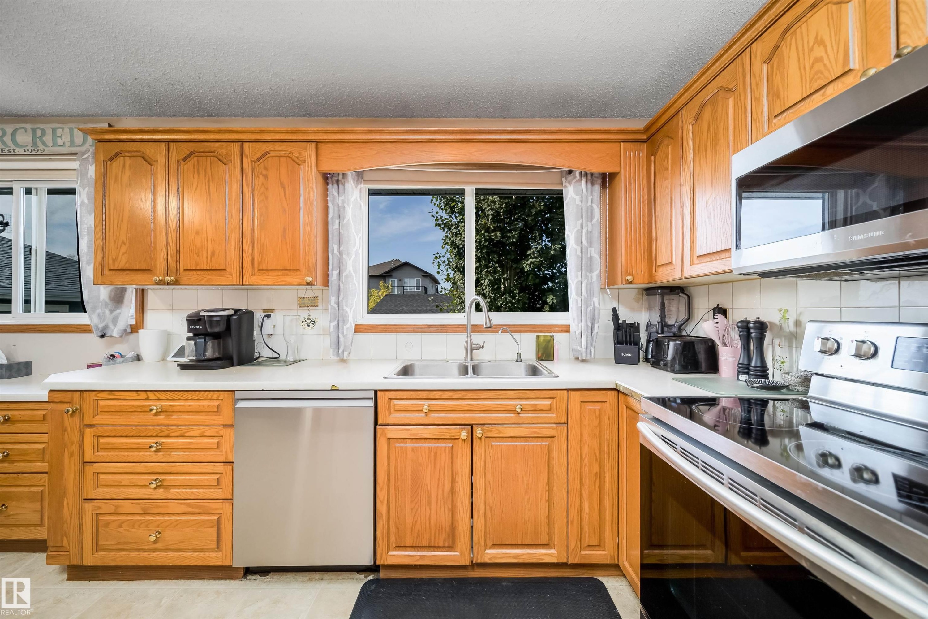 Wood-finish cabinetry, solid surface countertops, stainless steel appliances, and a double basin sink - 4104 44 Street, Stony Plain, AB