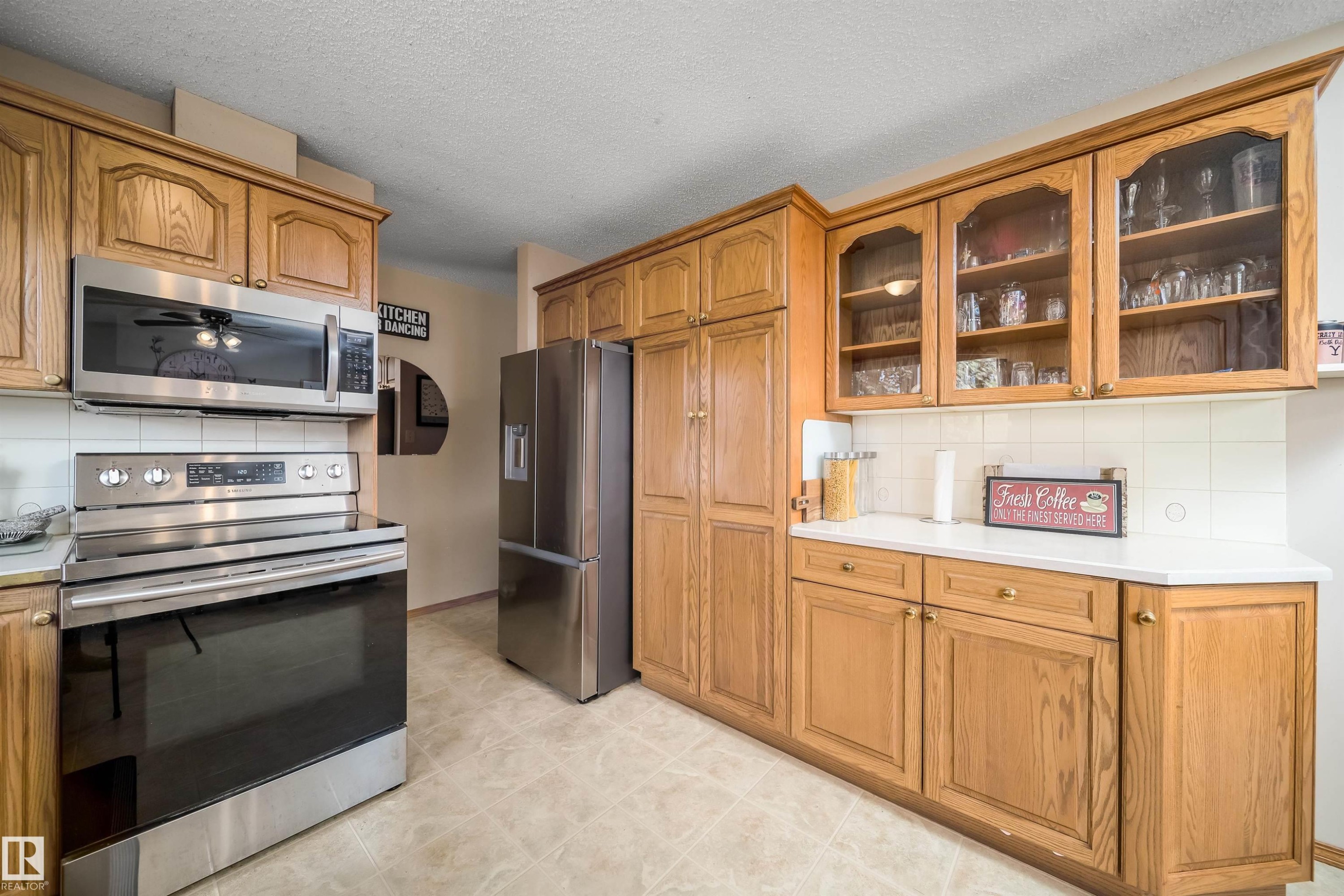Wood-finish cabinetry with glass-front uppers, stainless steel appliances, white countertops, and tiled backsplash - 4104 44 Street, Stony Plain, AB