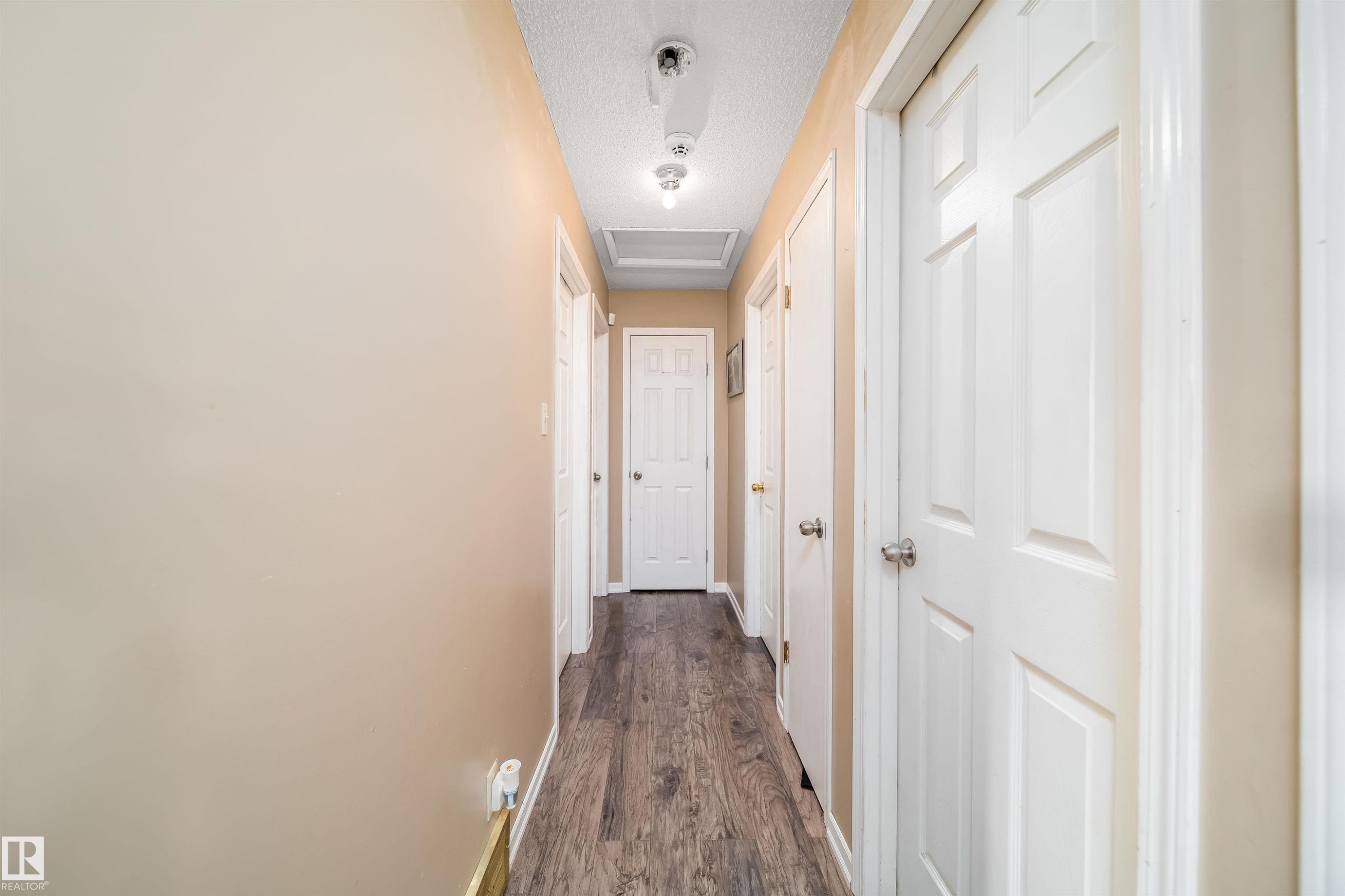 Hallway featuring wood-finish flooring, light neutral wall paint, white trim, and multiple panel doors - 4104 44 Street, Stony Plain, AB