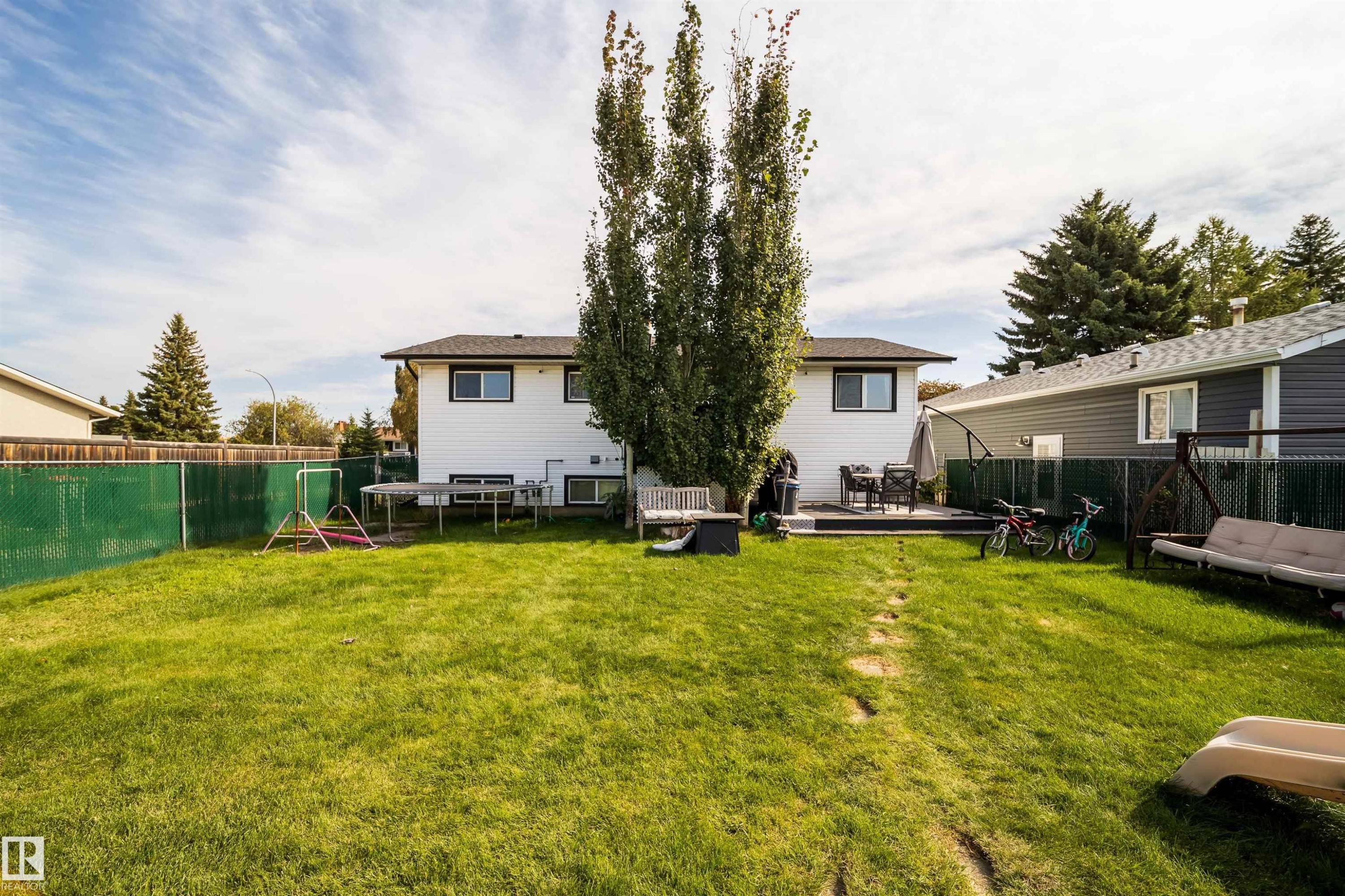 Expansive backyard with a manicured lawn, chain link fencing, a raised deck, and mature trees - 4104 44 Street, Stony Plain, AB