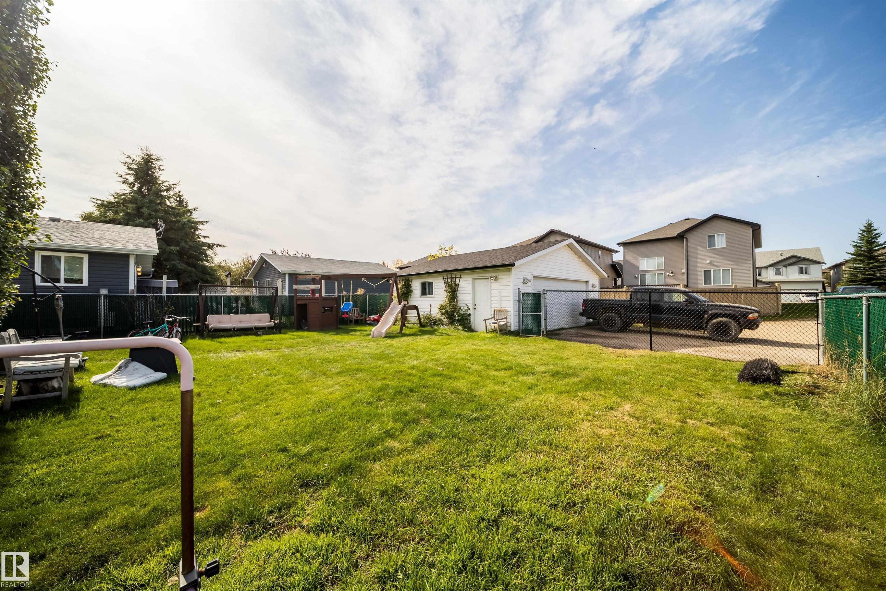 Expansive grass lawn with a chain-link fence, detached garage, and concrete parking pad - 4104 44 Street, Stony Plain, AB