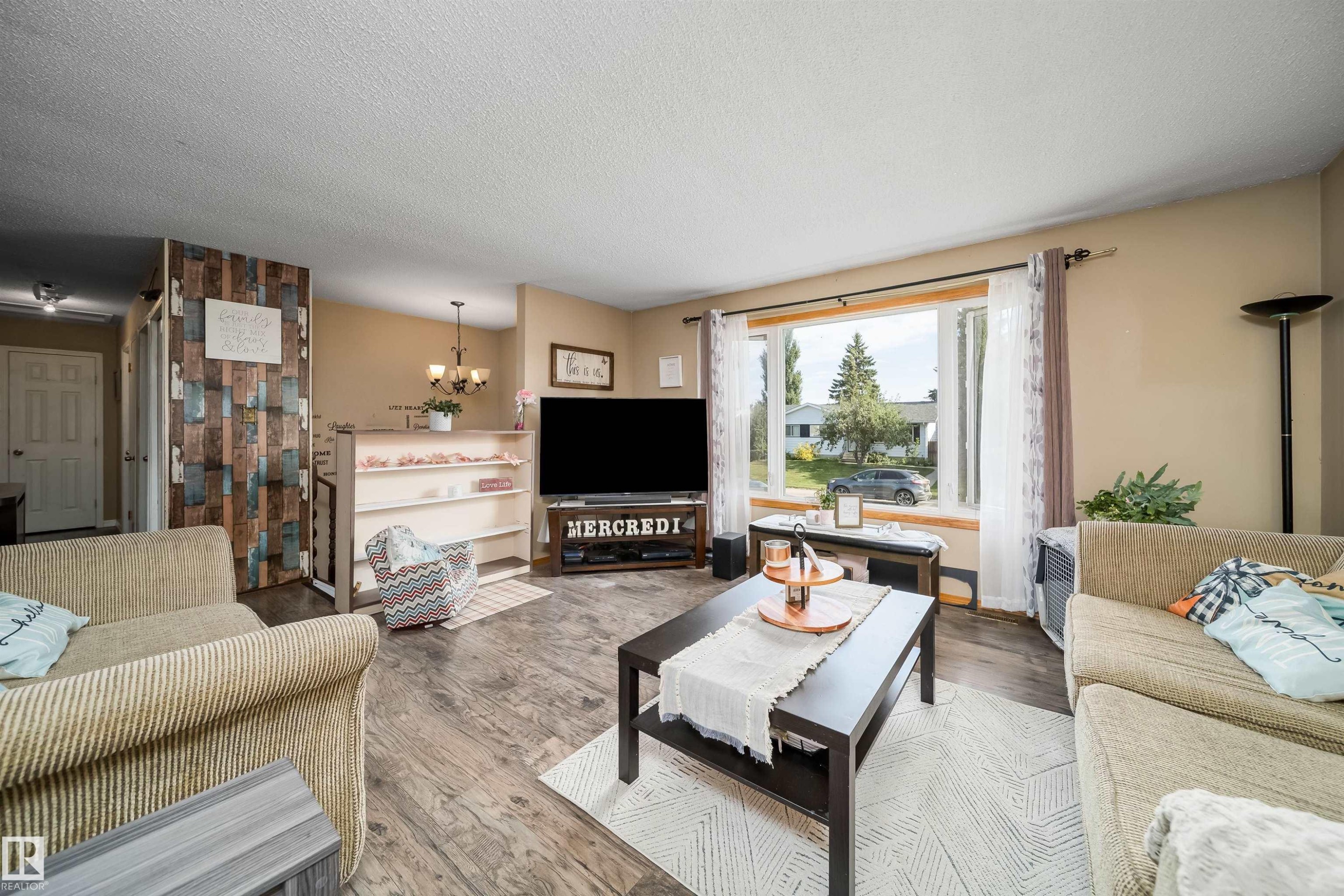 Expansive living area with wood-finish flooring, a large picture window, and neutral wall tones - 4104 44 Street, Stony Plain, AB