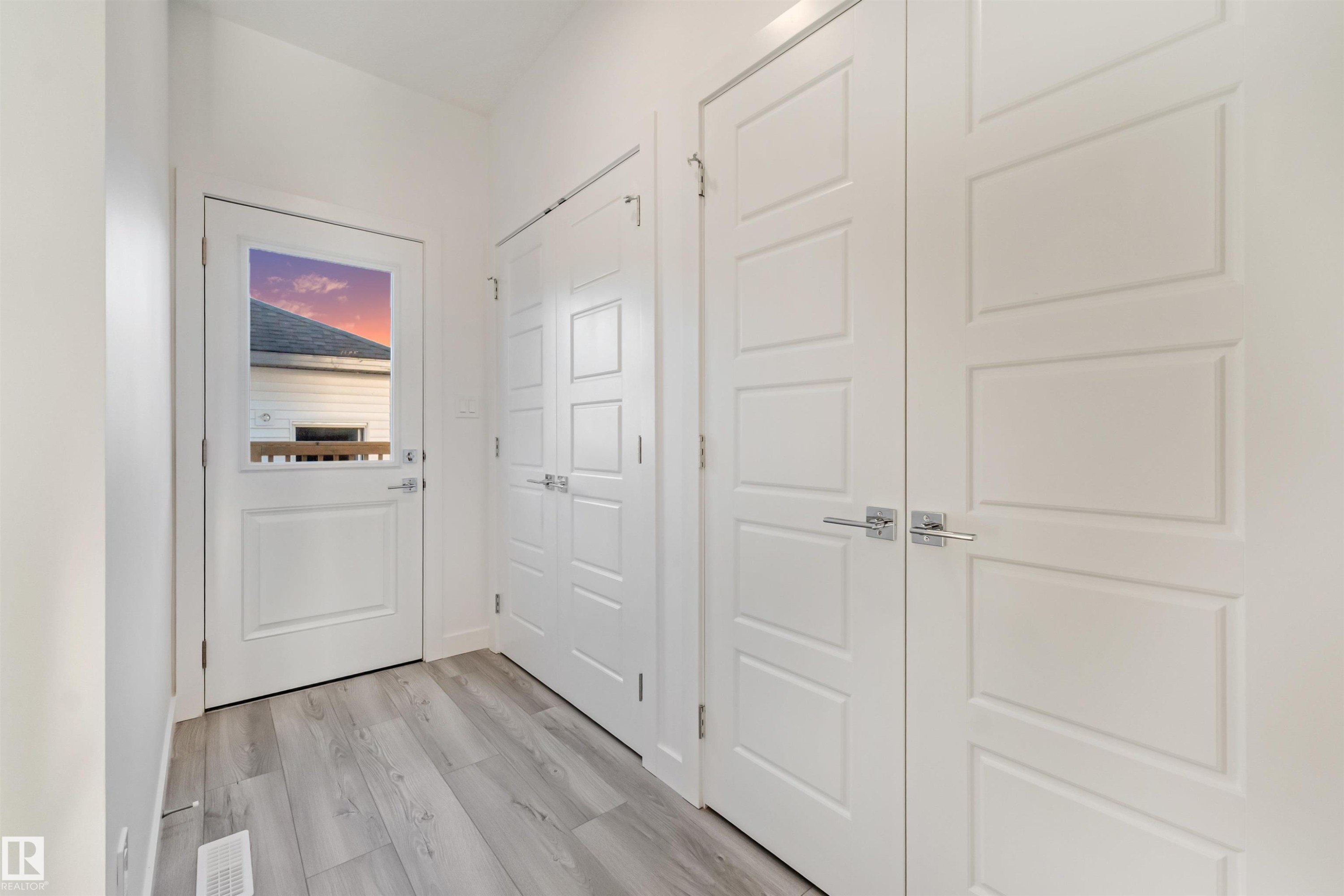 Entryway featuring light wood-finish flooring, white paneled doors with chrome hardware, and a glass-paneled exterior door - 1515 211 Street Nw, Edmonton, AB