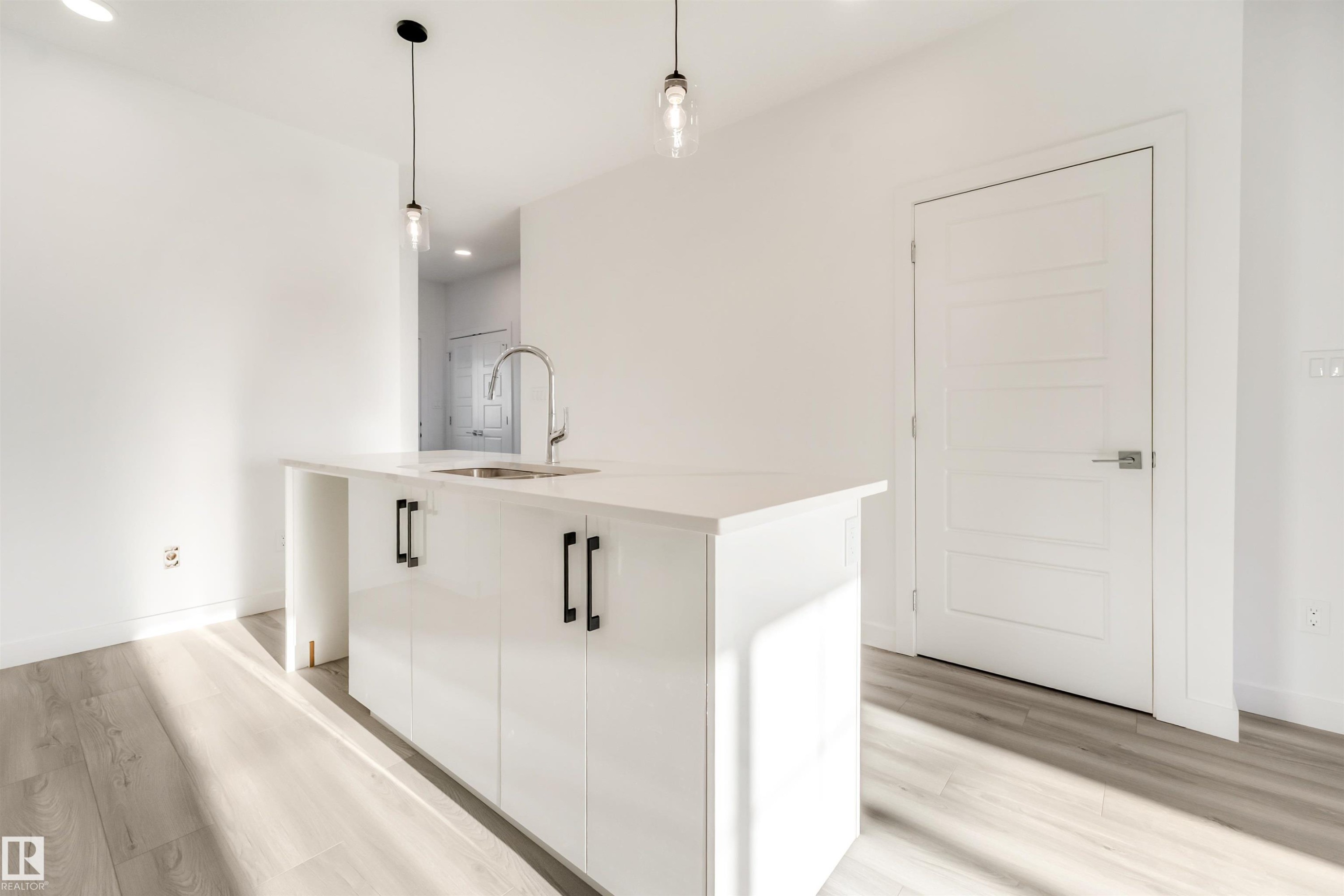 Kitchen island with a built-in sink, stainless steel faucet, and white cabinetry with matte black pulls - 1515 211 Street Nw, Edmonton, AB