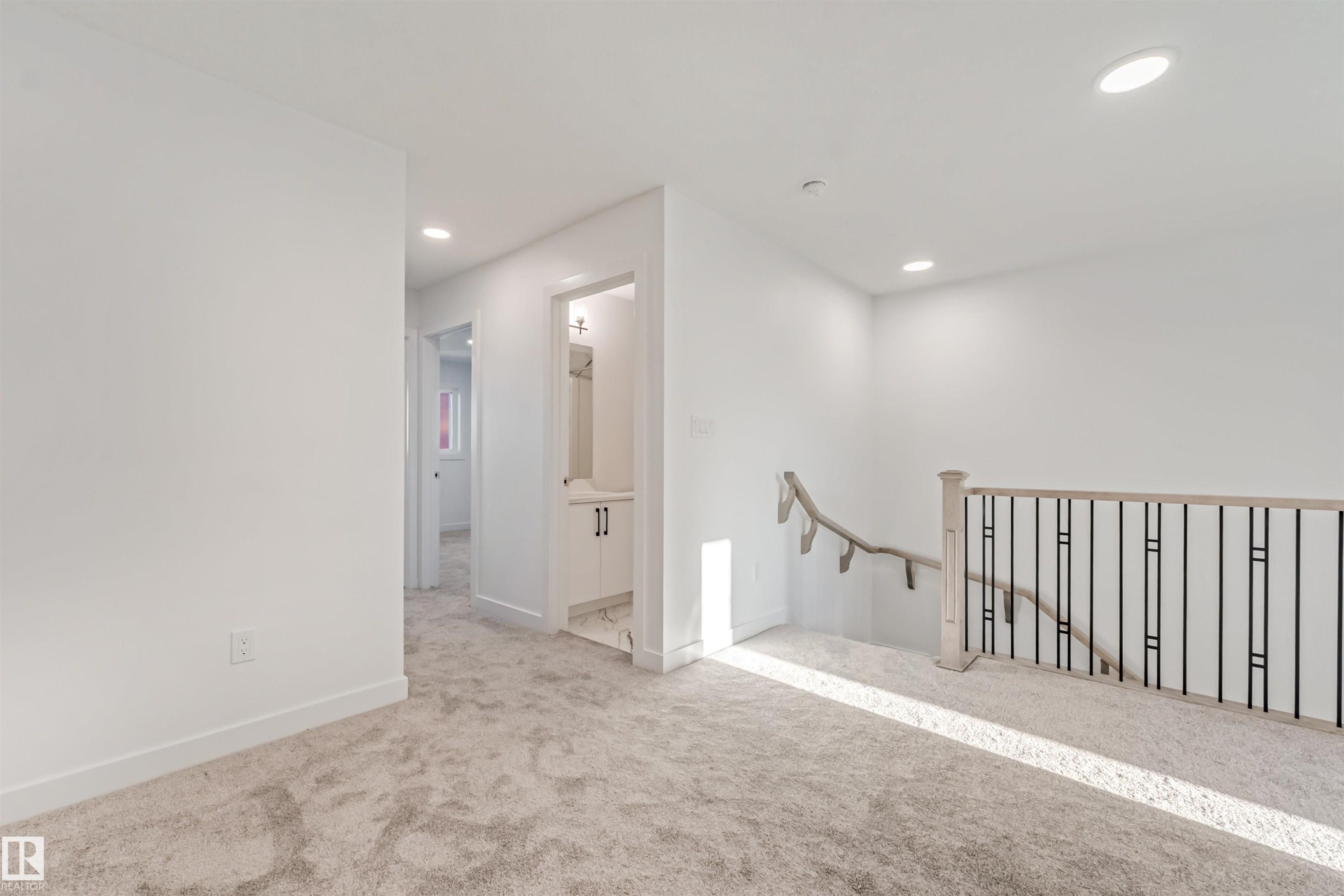 Carpeted landing with recessed lighting, white walls, and a staircase featuring black metal balusters and a light wood-finish handrail - 1515 211 Street Nw, Edmonton, AB