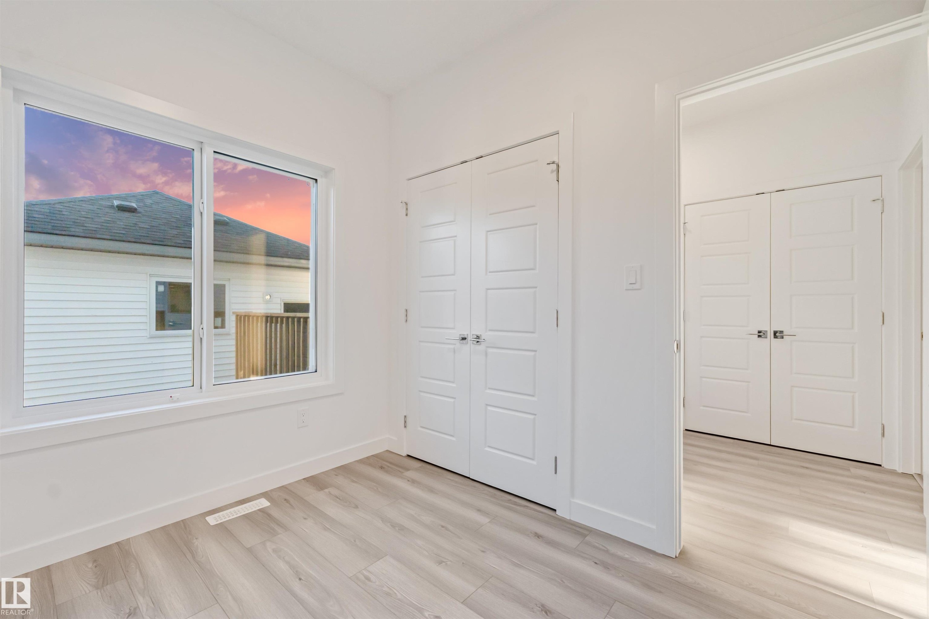 Expansive window with bright trim, light wood-finish flooring, and white paneled bi-fold doors - 1515 211 Street Nw, Edmonton, AB