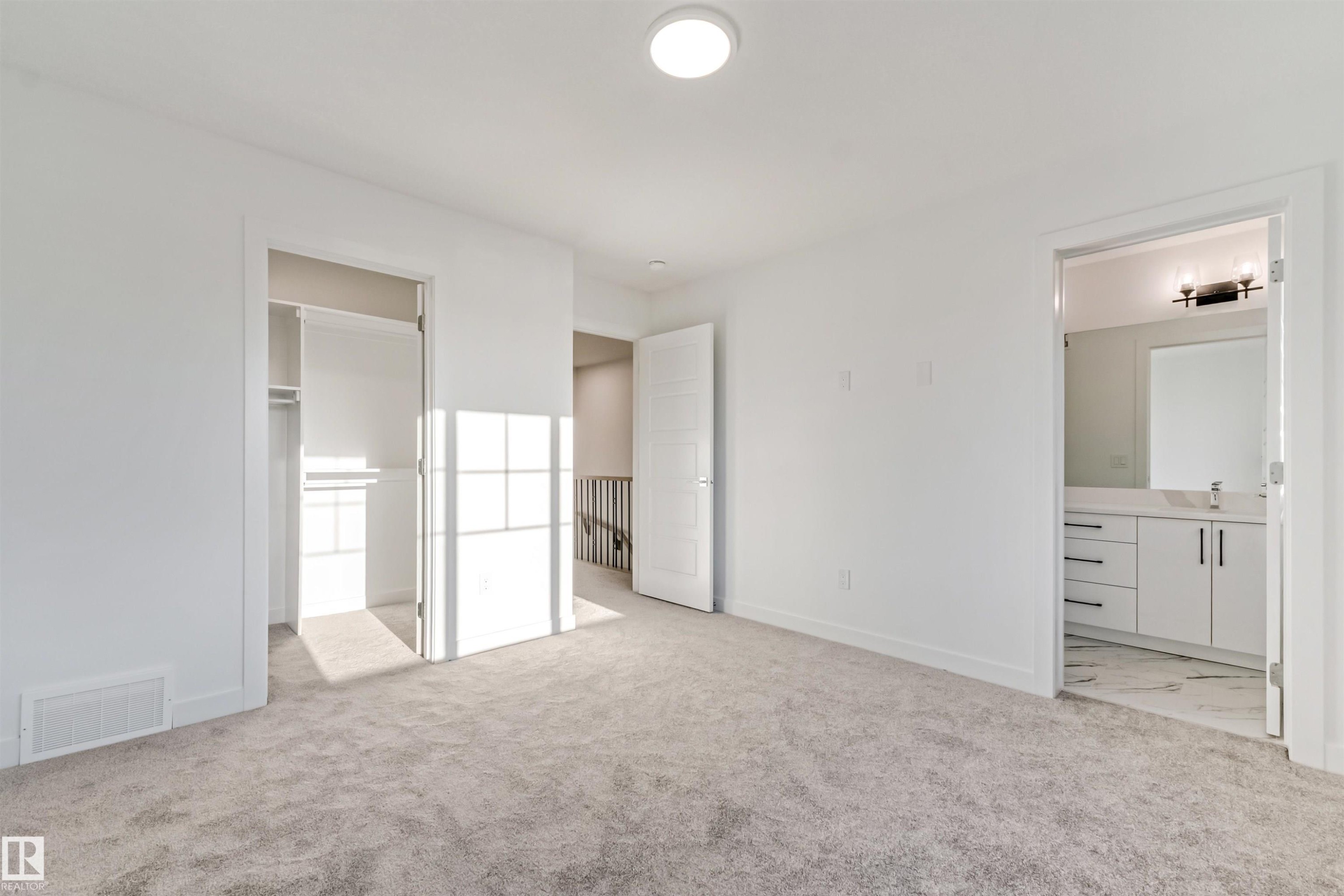 Carpeted room with white walls, an open closet, and a separate bathroom featuring a white vanity with a rectangular sink and a wall-mounted light fixture - 1515 211 Street Nw, Edmonton, AB