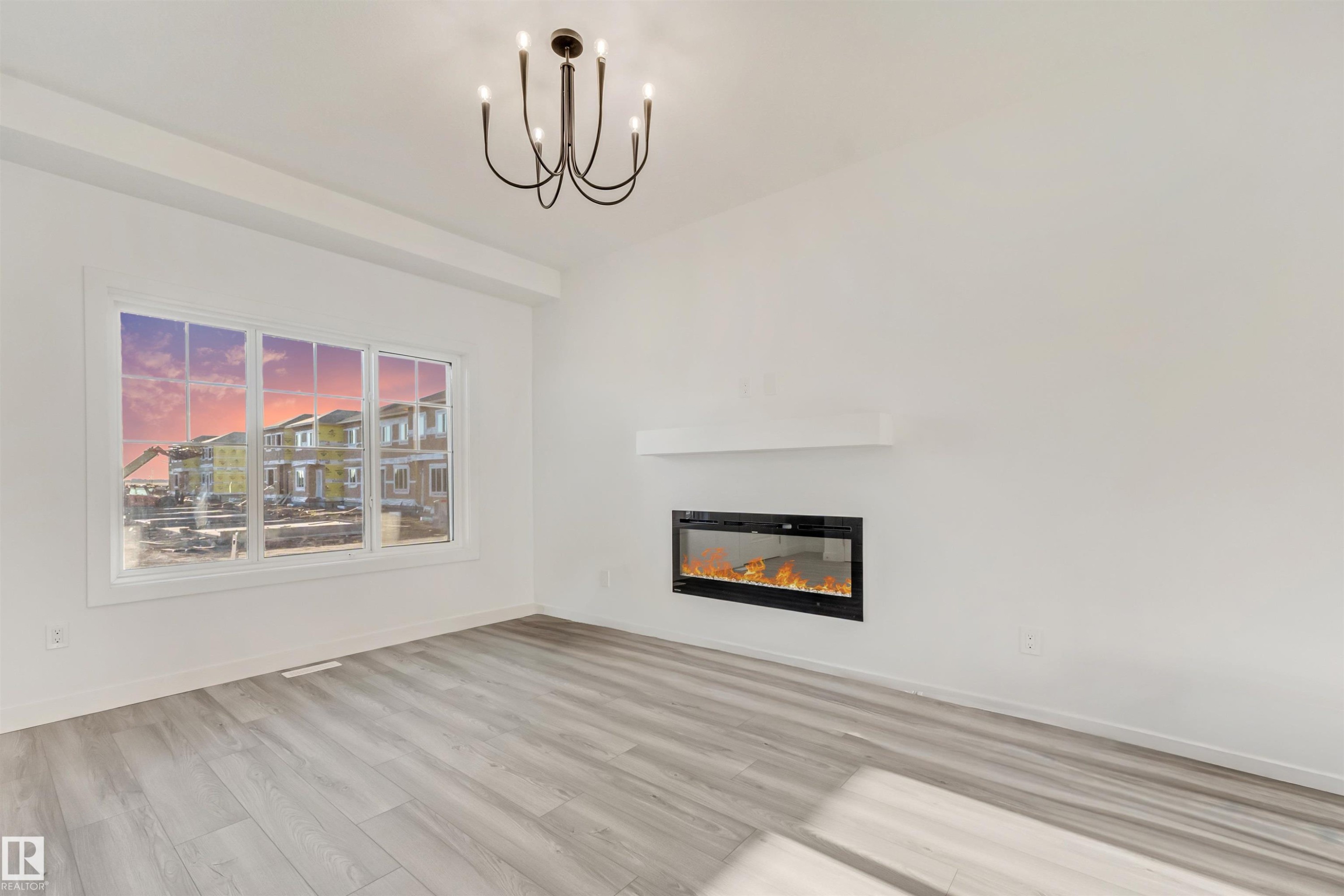Spacious room featuring wood-finish flooring, a contemporary chandelier, a built-in electric fireplace with a floating mantel, and multiple windows - 1515 211 Street Nw, Edmonton, AB