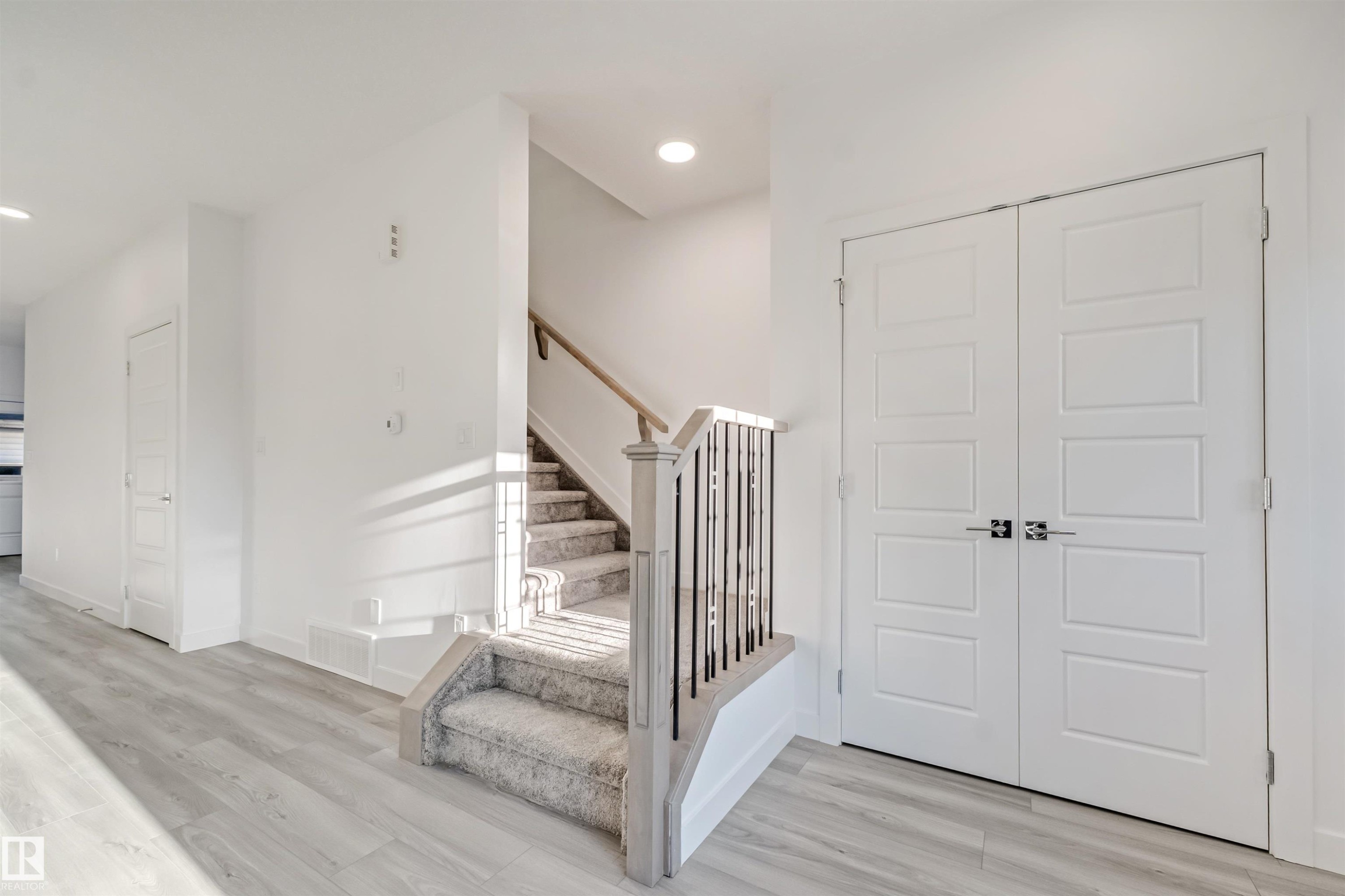 Wood-finish flooring with a carpeted staircase featuring a wood handrail and iron balusters - 1515 211 Street Nw, Edmonton, AB