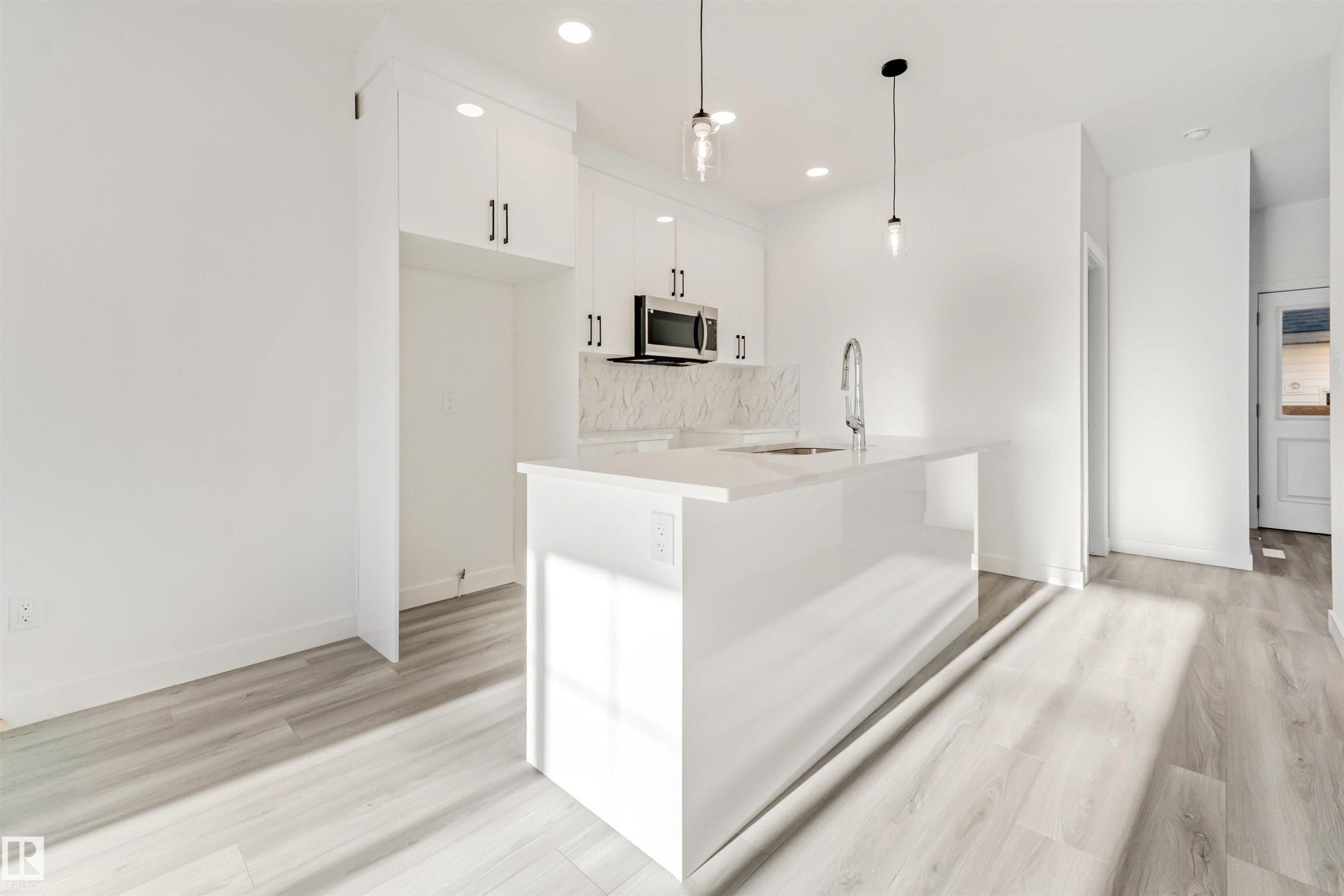 Modern kitchen featuring white cabinetry, a large island with an undermount sink, stainless steel microwave, and wood-finish flooring - 1515 211 Street Nw, Edmonton, AB