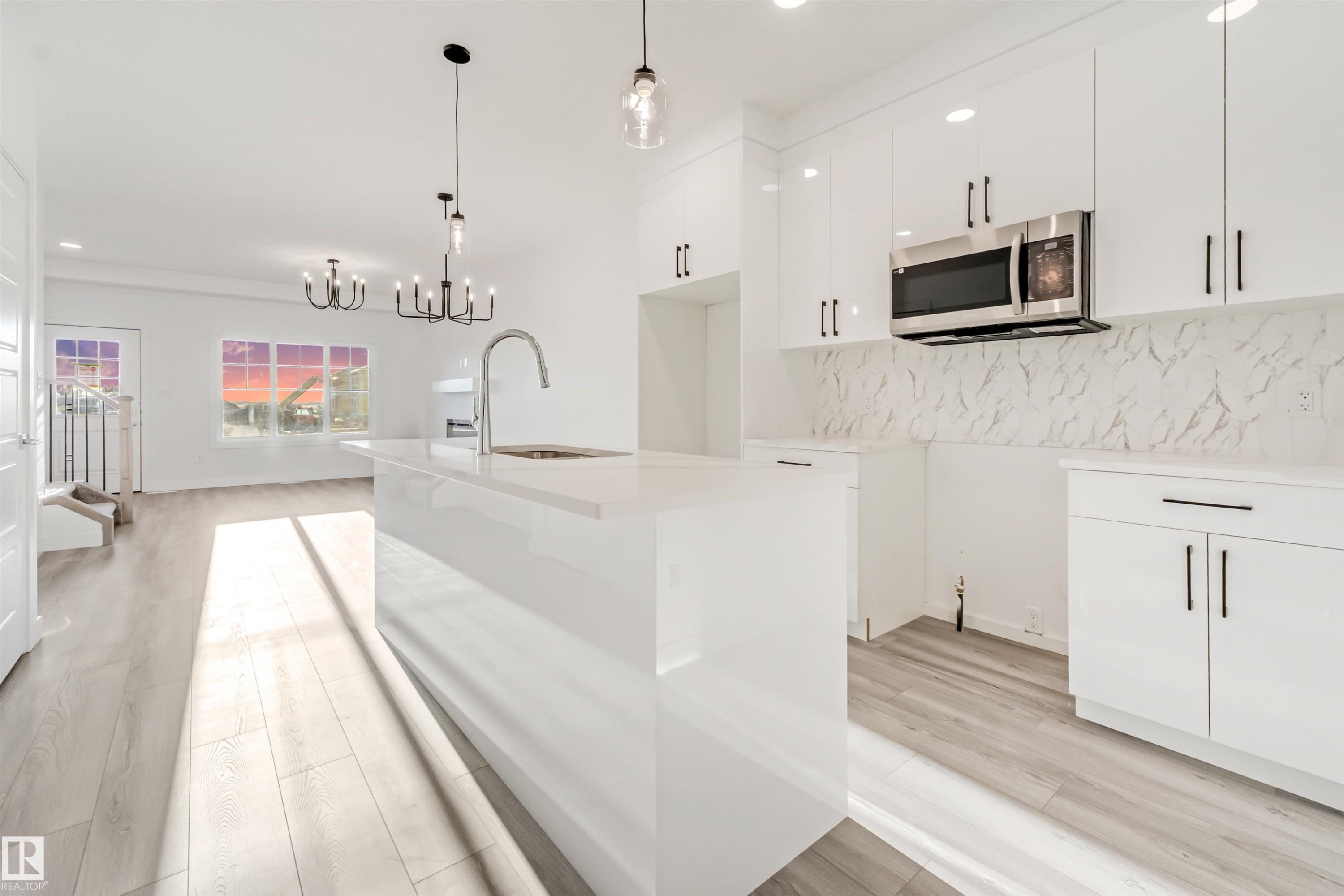 Modern kitchen featuring white cabinetry, a large kitchen island with an integrated sink, and stainless steel microwave - 1515 211 Street Nw, Edmonton, AB
