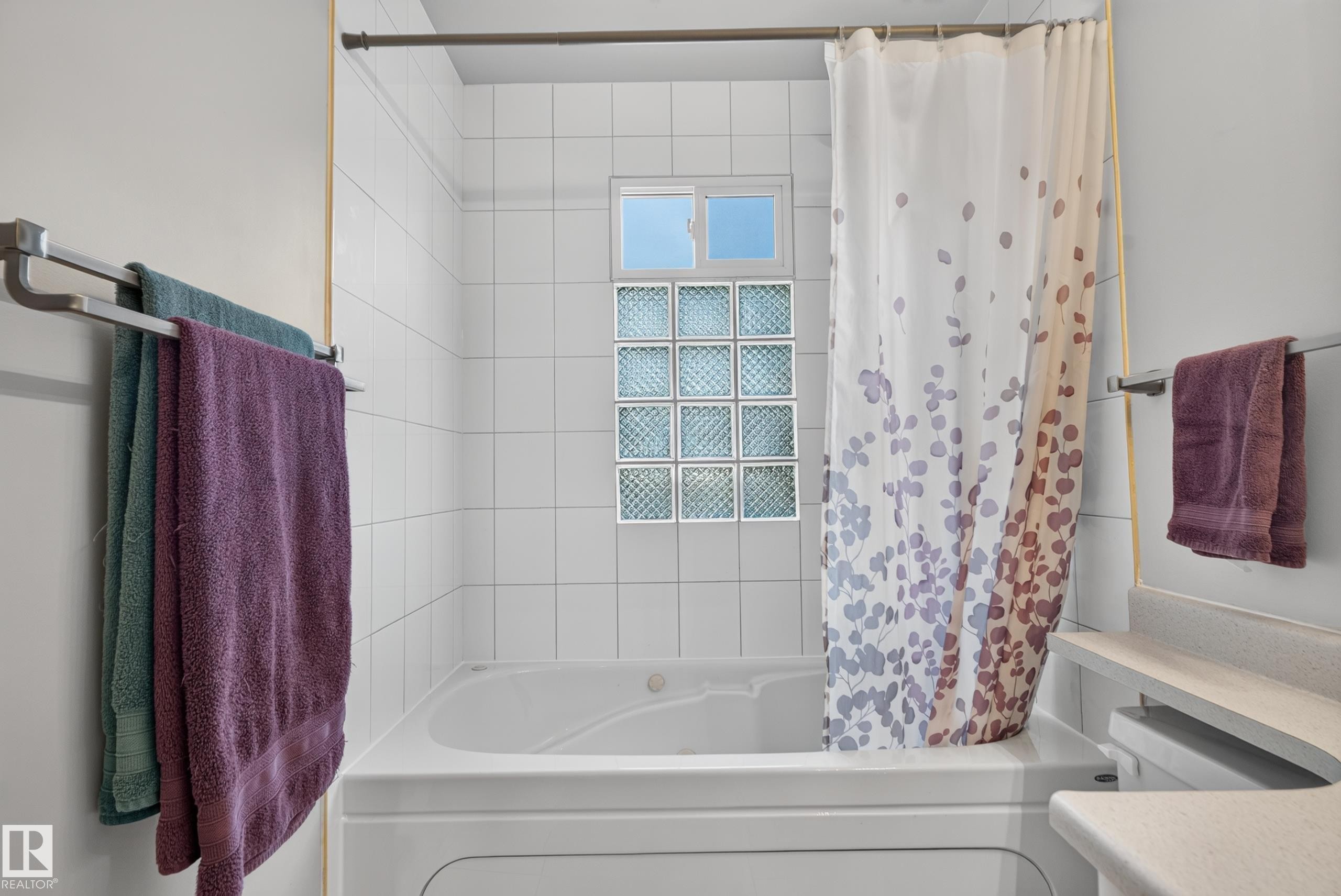 White tiled bath surround with an integrated bathtub, glass block window, and upper window - 14611 109 Avenue Nw, Edmonton, AB