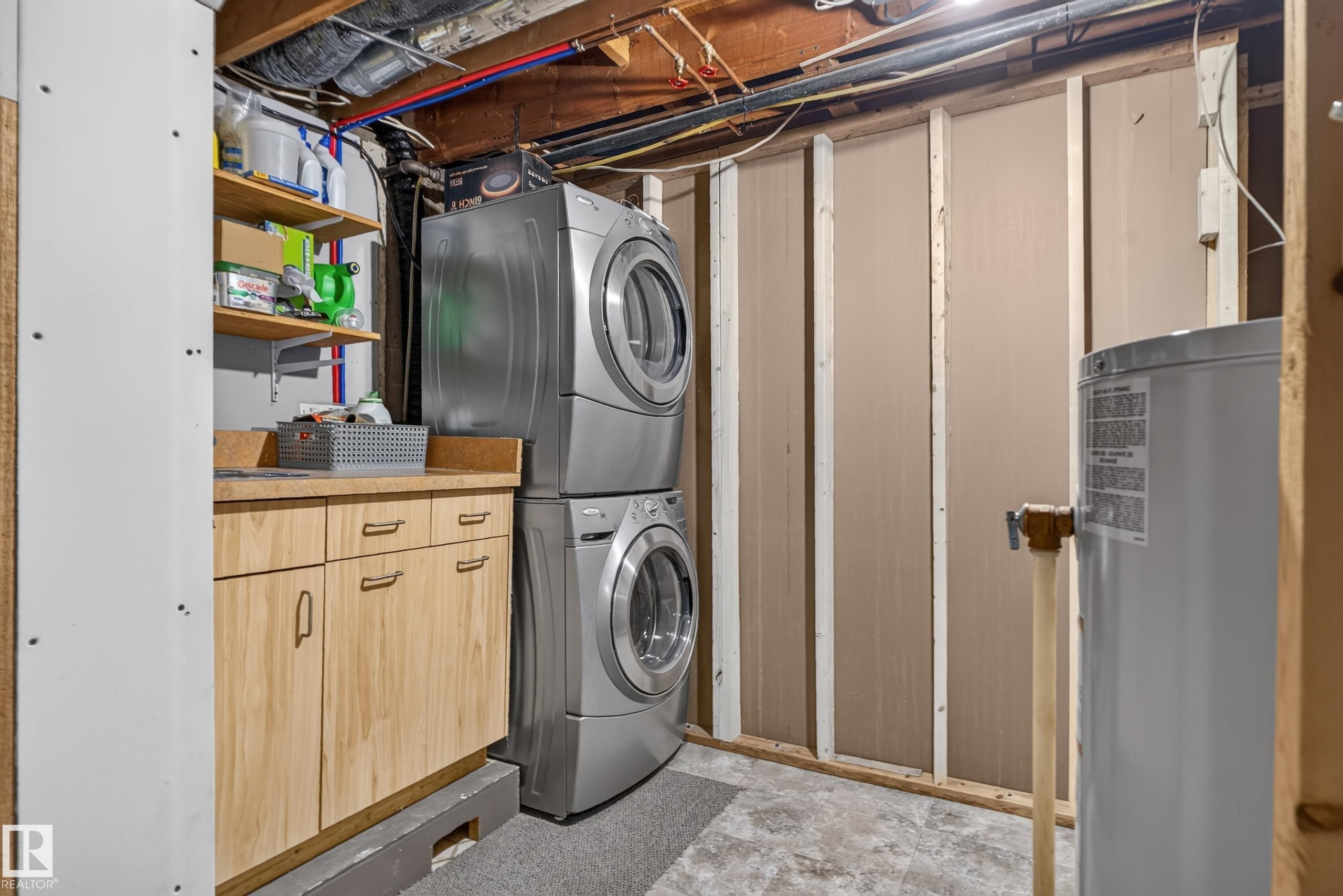 Stackable laundry appliances, wood-finish cabinetry, built-in shelving, laminate countertop, and water heater - 14611 109 Avenue Nw, Edmonton, AB