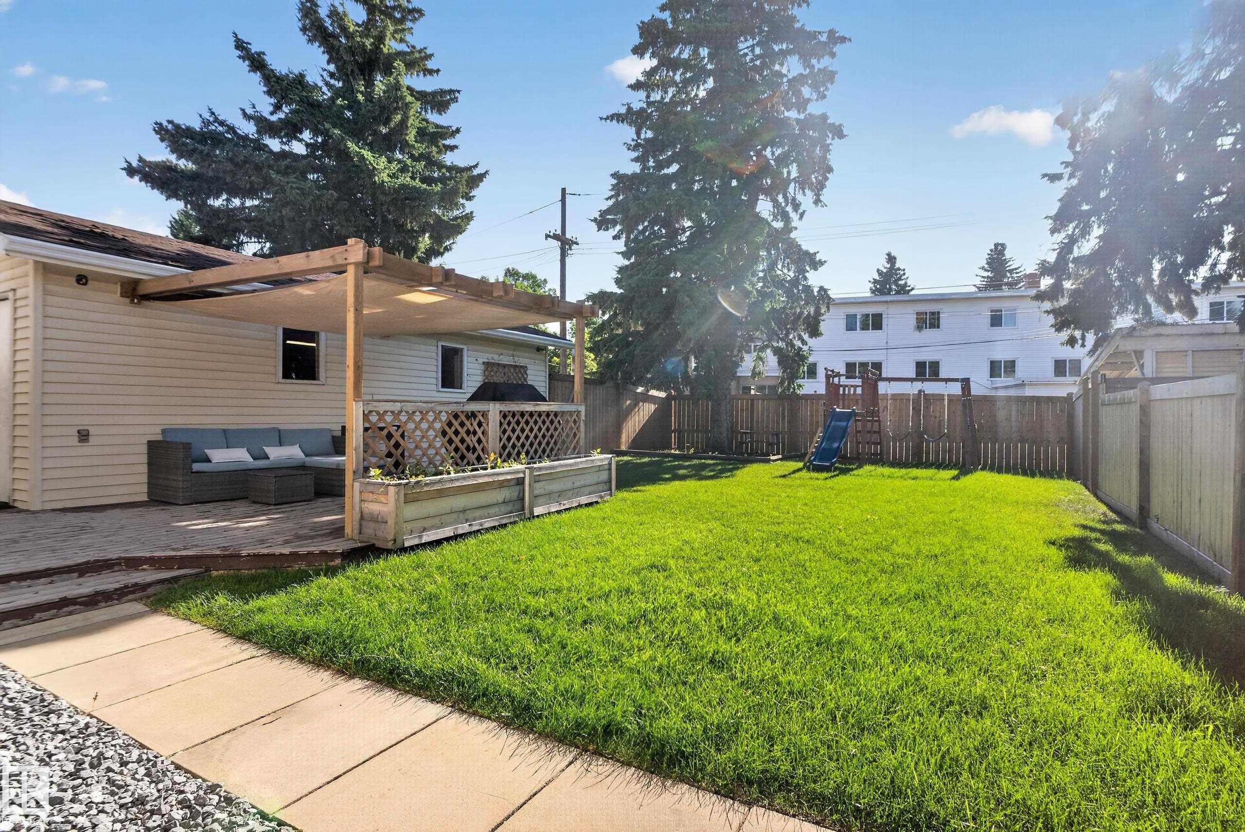 Expansive backyard featuring a manicured lawn, wood fencing, and a paved patio area - 14611 109 Avenue Nw, Edmonton, AB