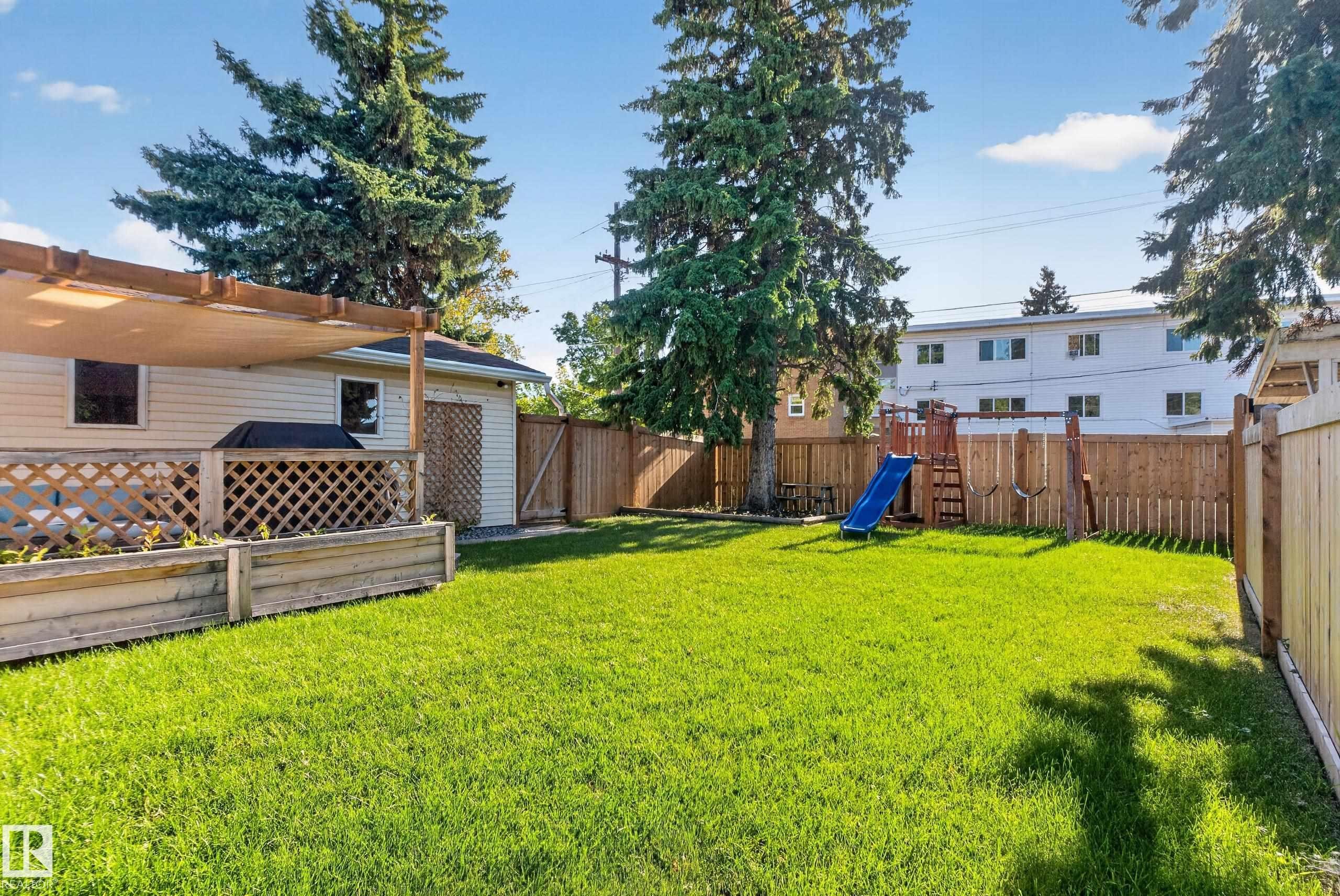 Expansive grassy yard with wood fencing, mature trees, and a detached structure with an attached pergola - 14611 109 Avenue Nw, Edmonton, AB
