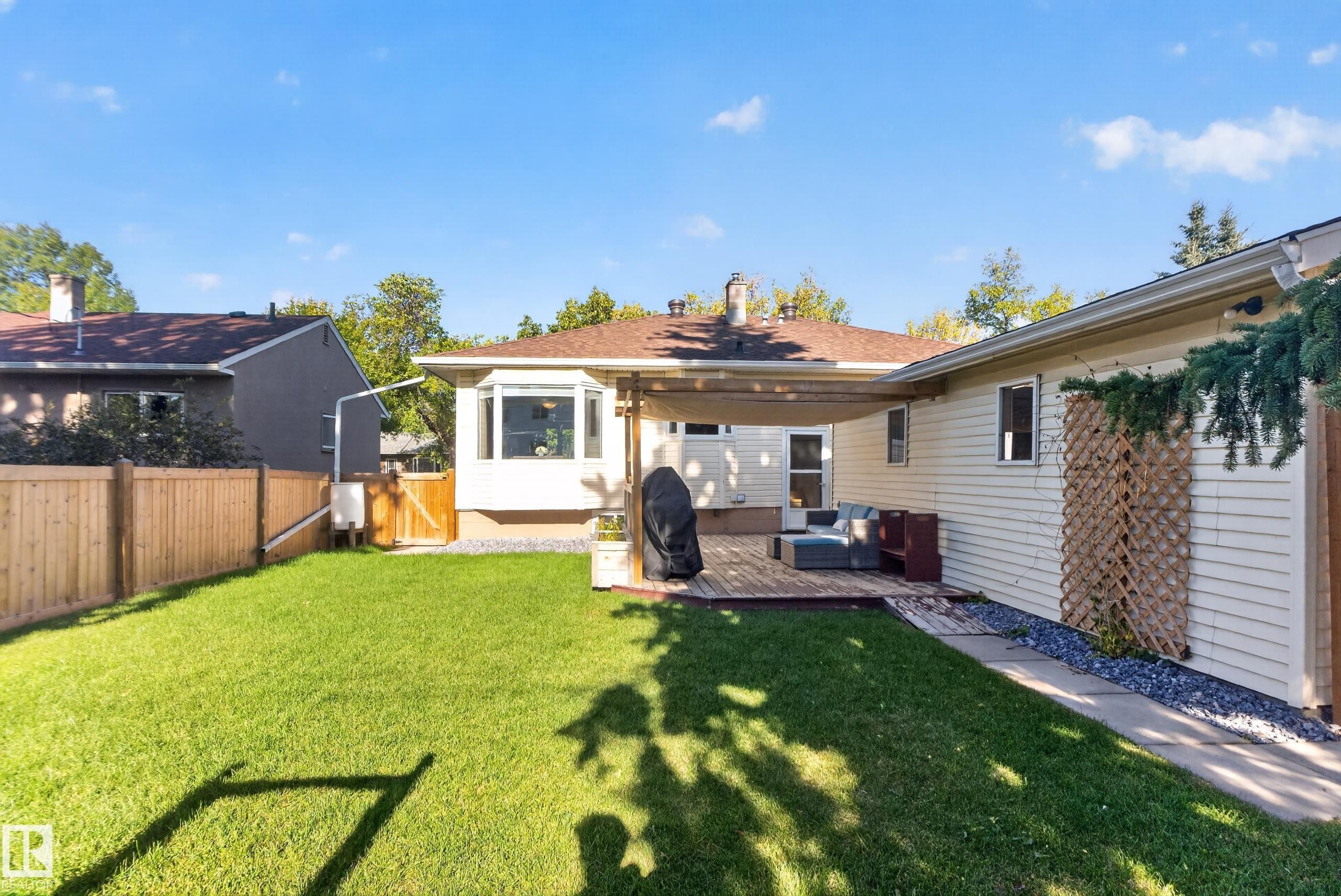 Expansive backyard featuring a manicured lawn, wood privacy fence, multi-level wood decking, and a bay window - 14611 109 Avenue Nw, Edmonton, AB