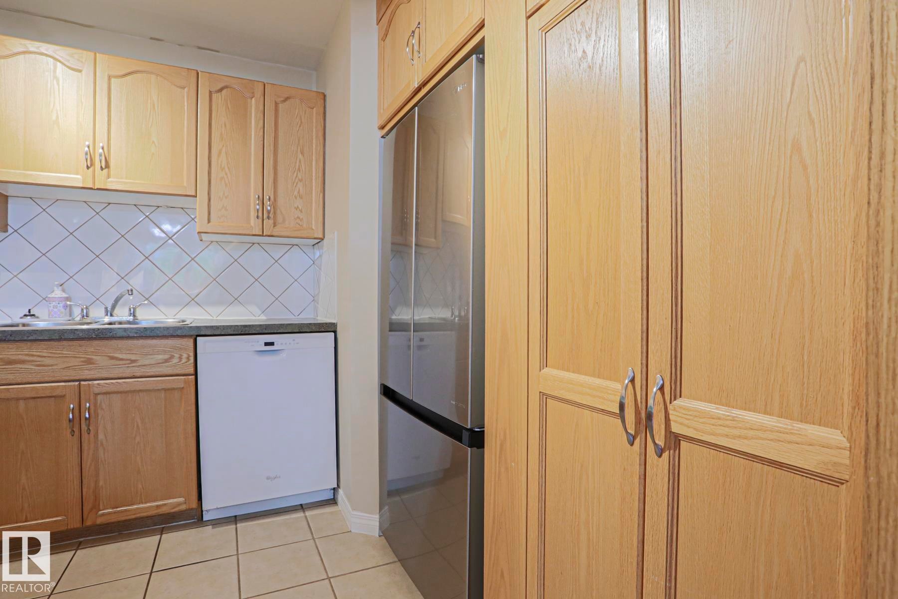 Wood-finish cabinetry, stainless steel refrigerator, white tile backsplash, and ceramic tile flooring - 319 Telford Court, Leduc, AB
