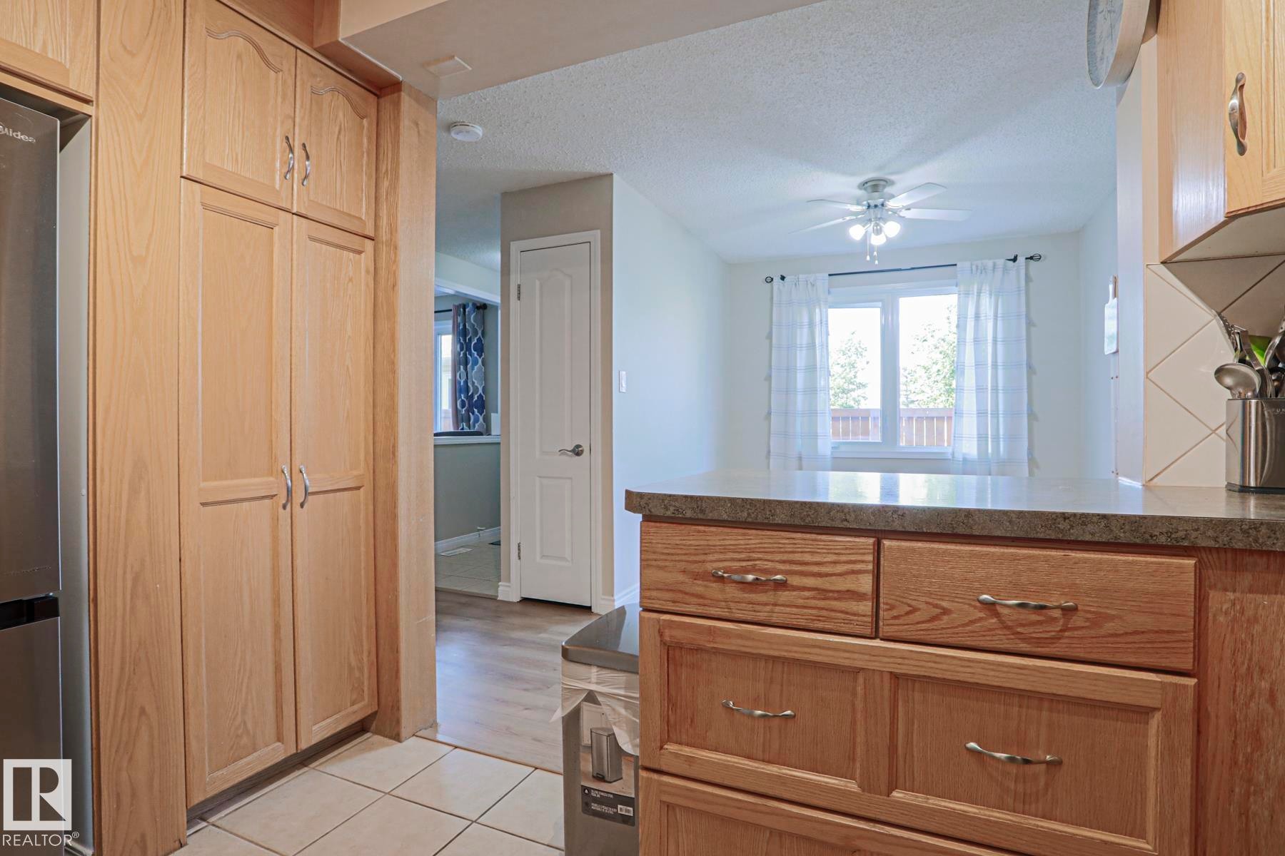Light wood-finish cabinetry, tile flooring, wood-finish flooring, and a ceiling fan - 319 Telford Court, Leduc, AB